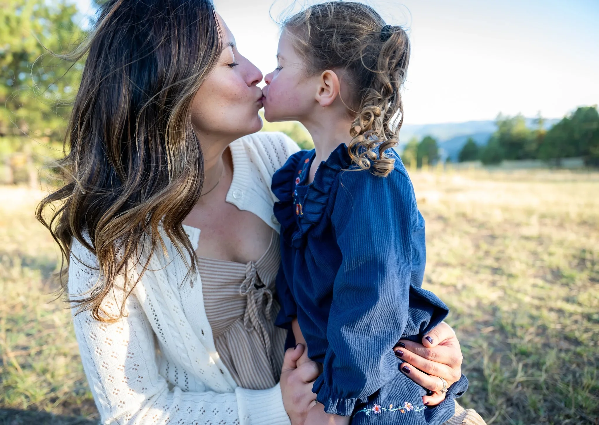 Mom & daugter share a sweet kiss during a relaxed outdoor family photo session at Mount Falcon West Trailhead in the Denver Foothills. Ryan Kost Photography.