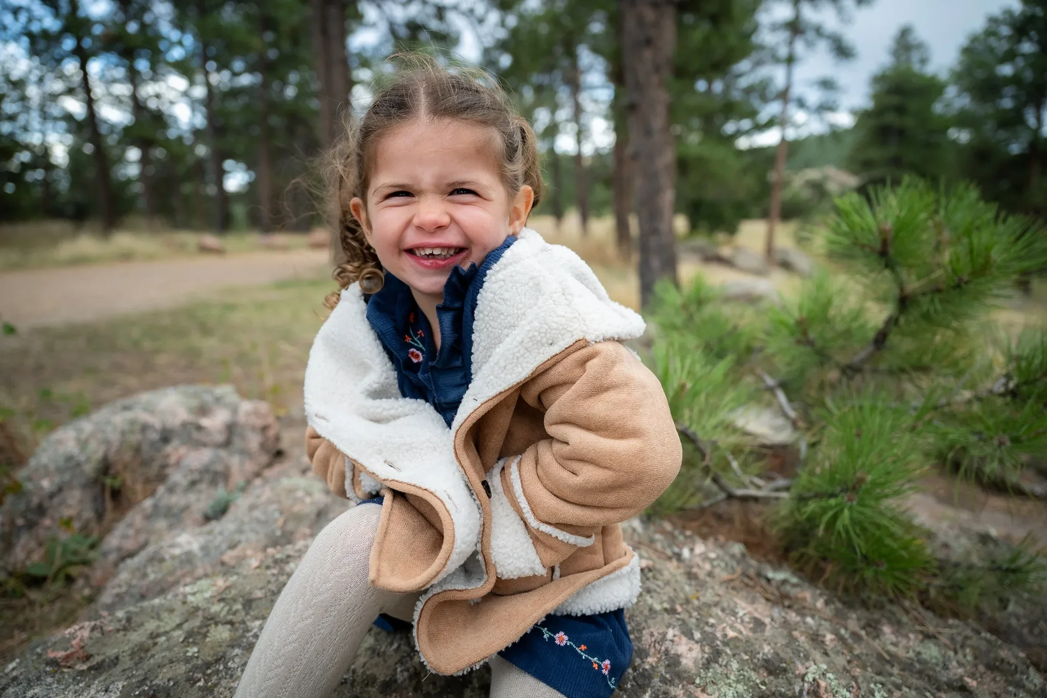 A sweet, natural portrait of young girl sitting on rock outcropping at Mount Falcon West during a relaxed Colorado fall family photo session captured by Ryan Kost