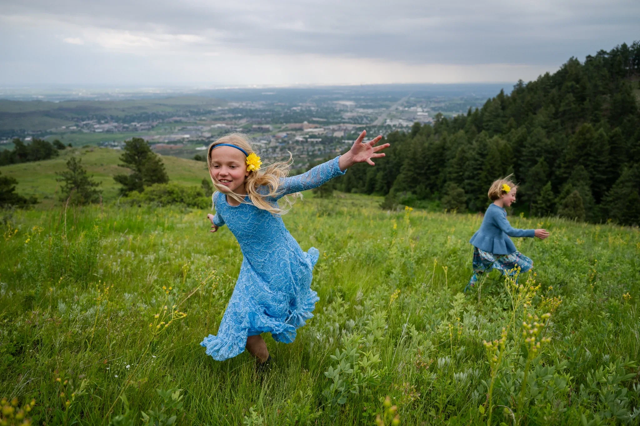 Sisters joyfully running through a summer green meadow on Lookout Mountain in Golden, Colorado. Ryan Kost Photography