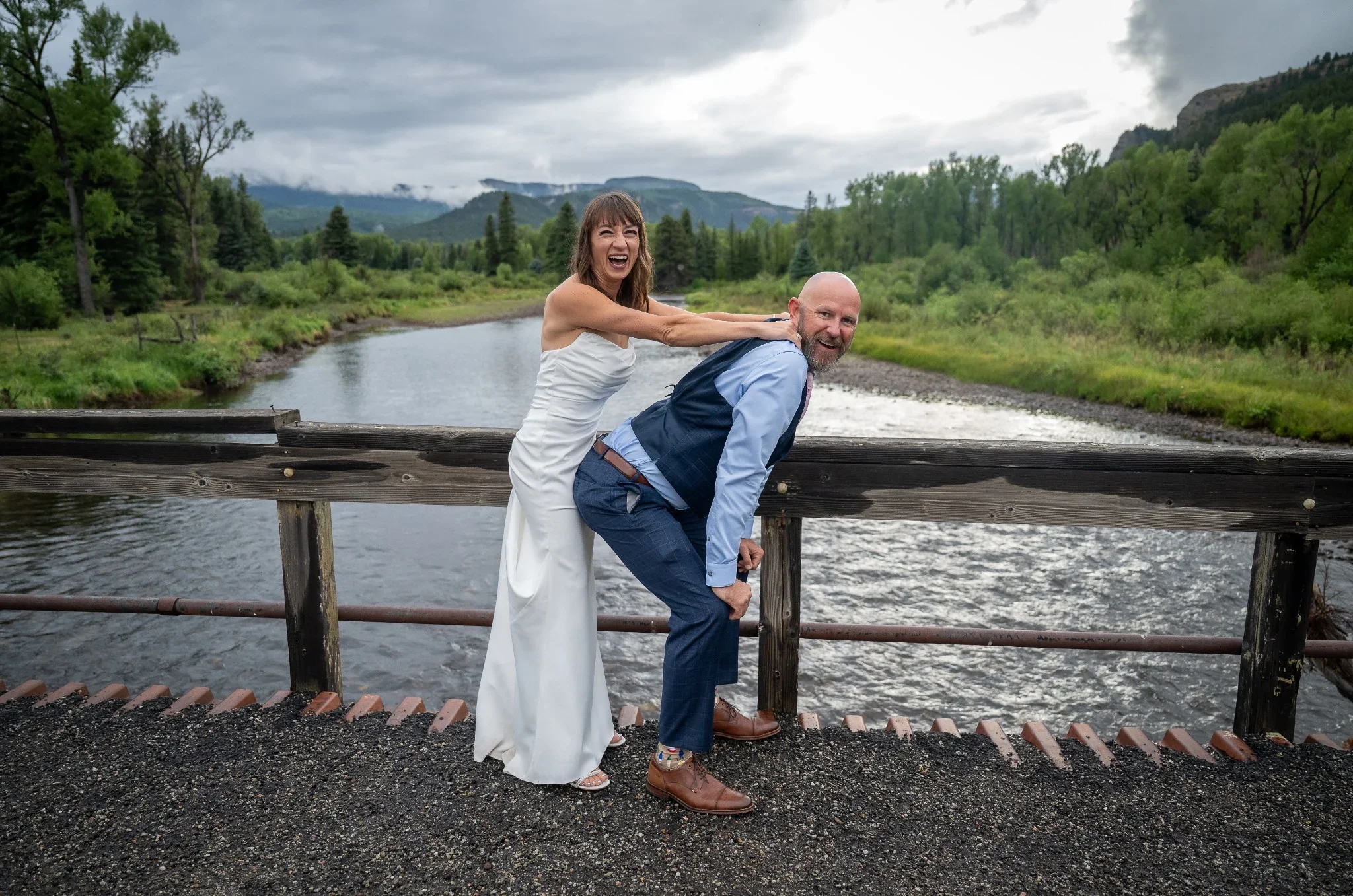 Bride and Groom getting silly on old bridge above Conejos River in Horca, Colorado. Wedding photography captured by Ryan Kost.
