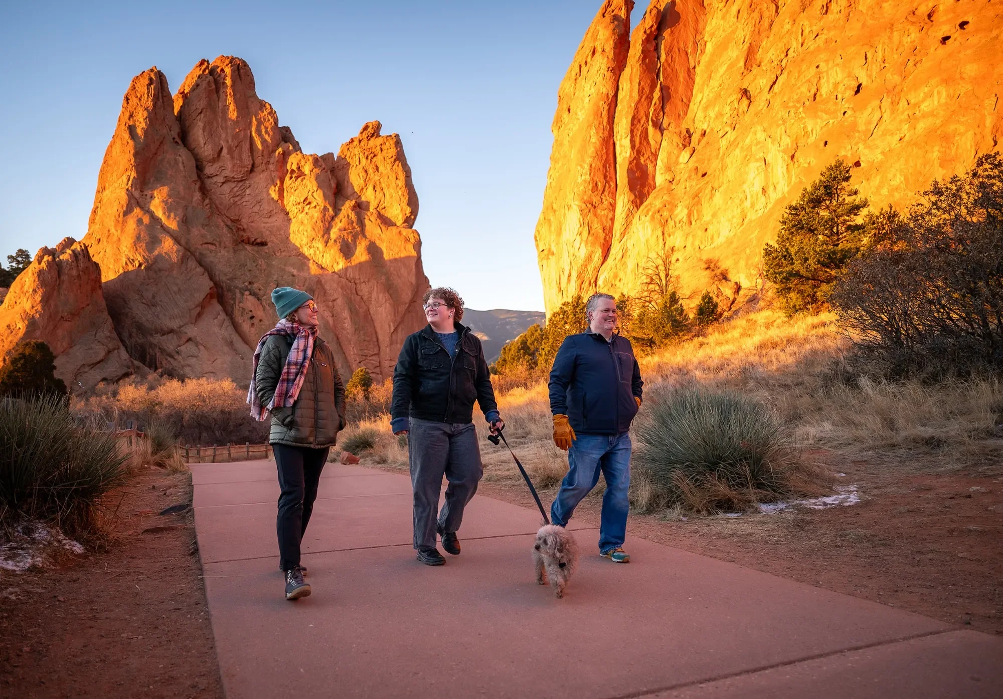 Family walking with dog on path during sunrise at Garden of the Gods. High school senior portrait session by Ryan Kost.