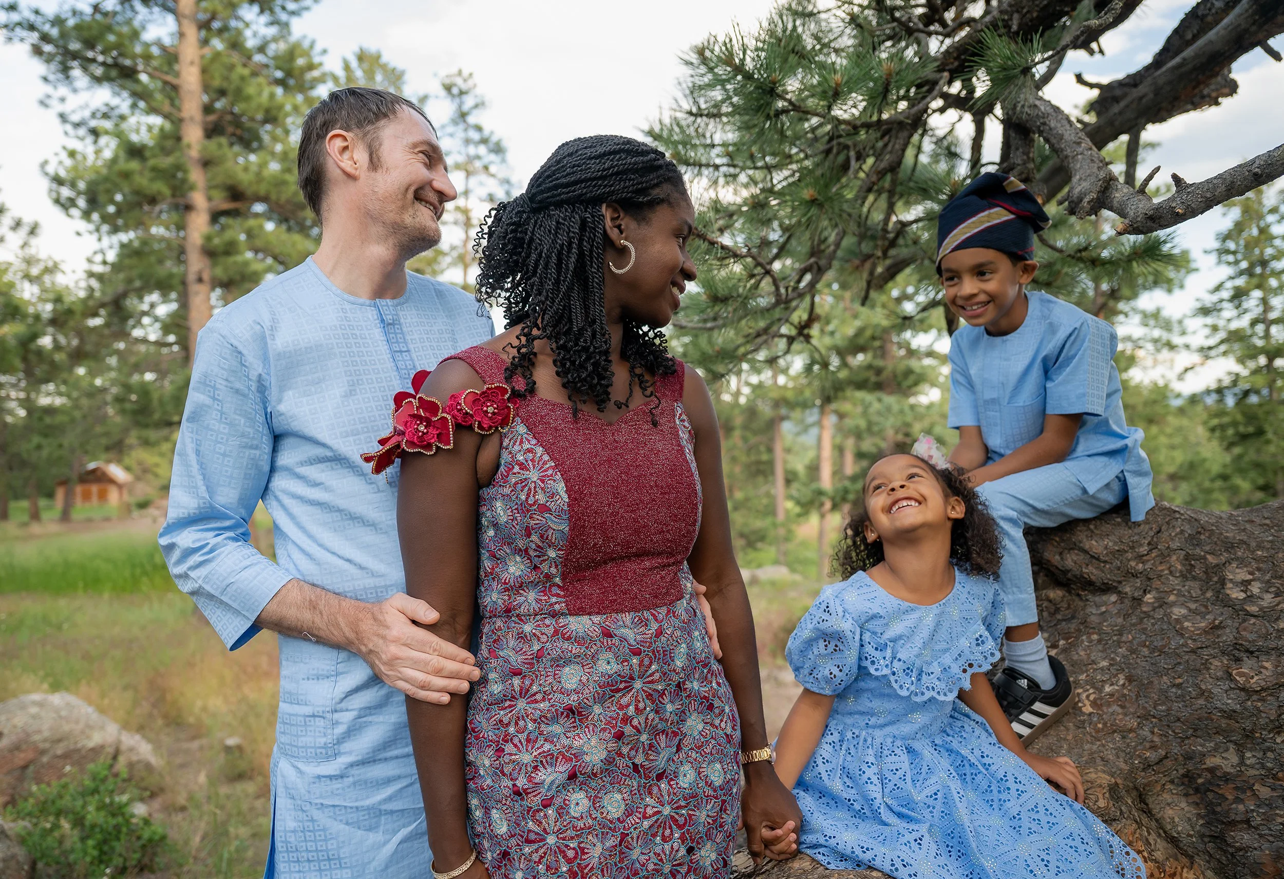 Childrensitting on tree smiling up at parents. Genuine, natural and authentic family photography at Mount Falcon West Trailhead Indian Hills, Colorado captured by Ryan Kost.