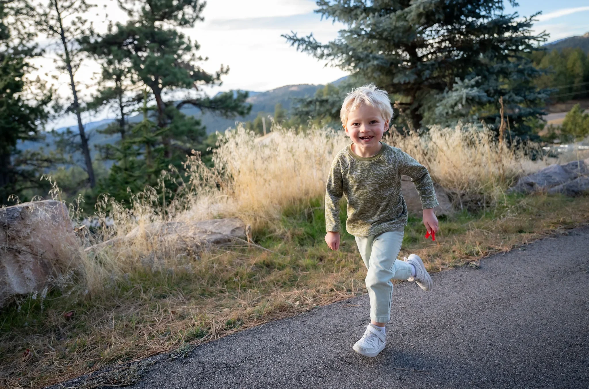 Young child smiling and running outdoors with pine trees and foothills in the background, Indian Hills CO