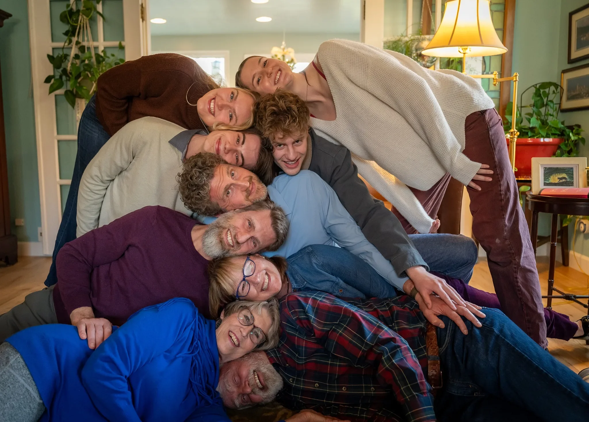 Denver in-home documentary family photo session featuring a large multi-generational family in a playful head-stacking portrait, photographed by Ryan Kost