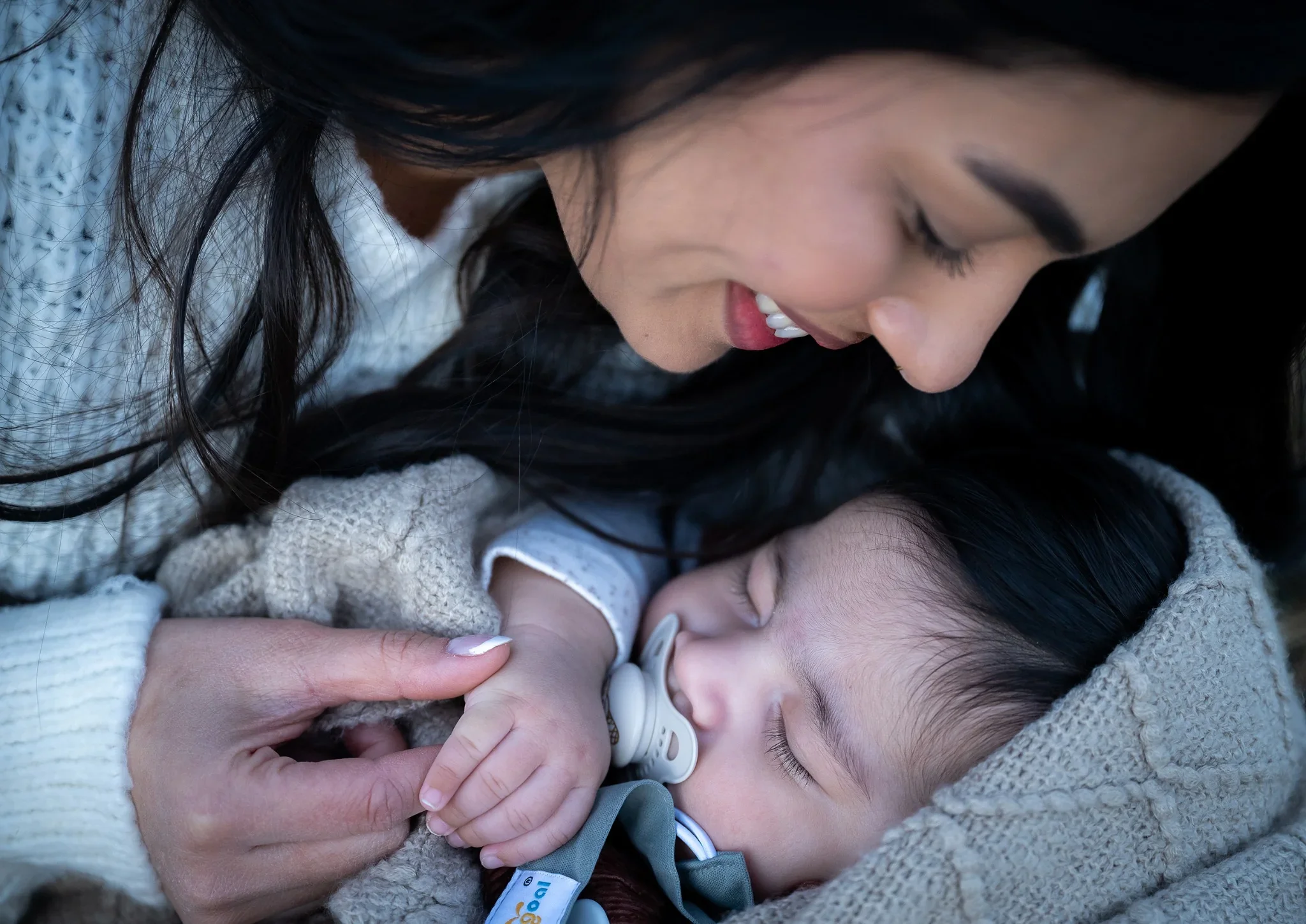 Mother smiling down at her newborn baby wrapped in a blanket during a cozy outdoor family session at South Valley Park in Littleton— captured by Ryan Kost, Colorado family photographer.