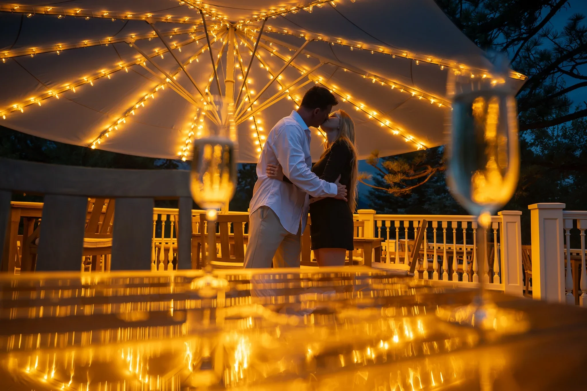 Engaged couple kissing beneath glowing patio lights at the Stanley Hotel in Estes Park, Colorado