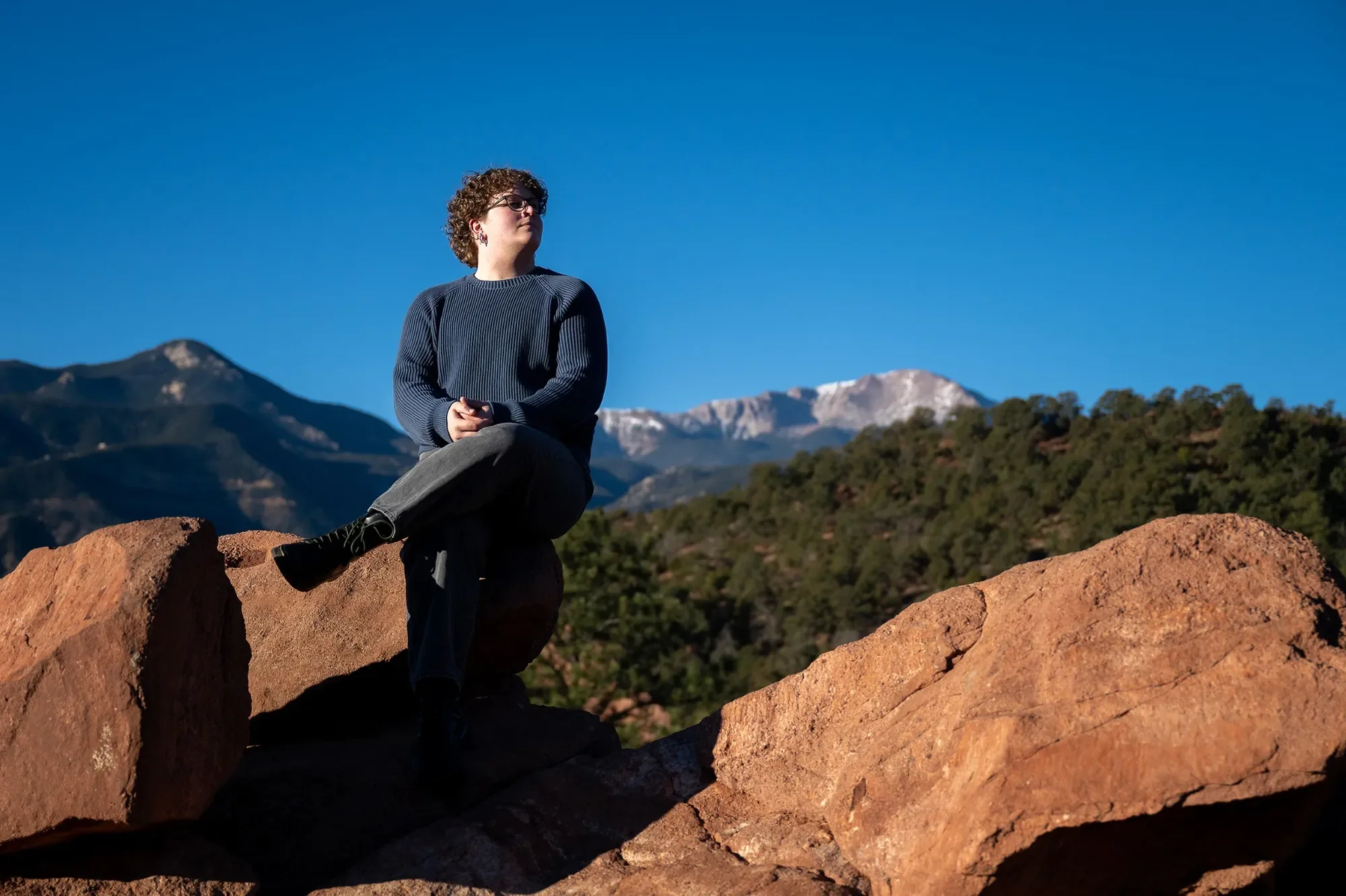 High school senior portrait sitting on red rocks with Pikes Peak behind. Garden of the Gods, Colorado Springs.