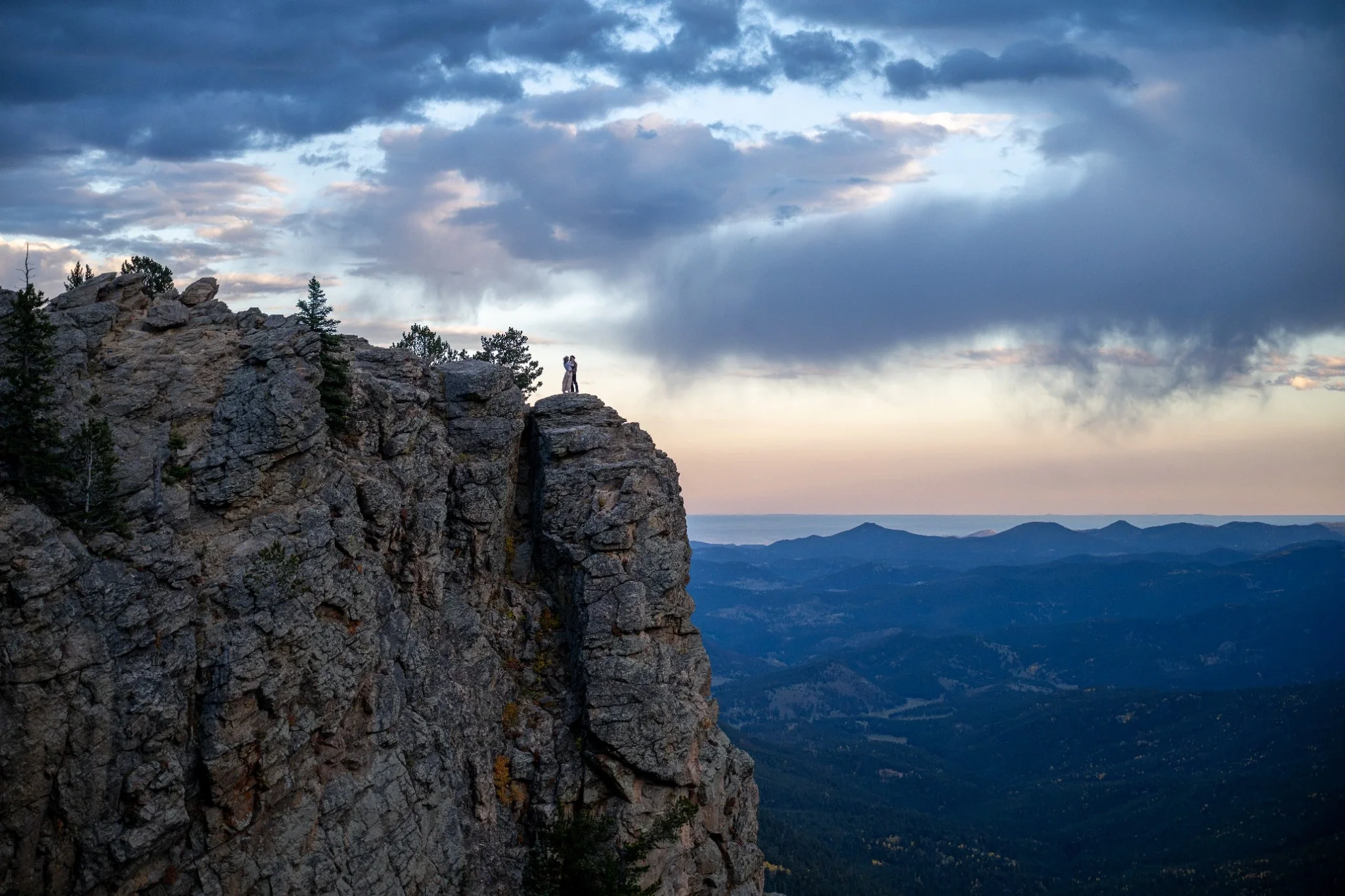 A couple embraces high atop a cliff at Juniper Pass in the foothills. Colorado engagement photographer Ryan Kost.