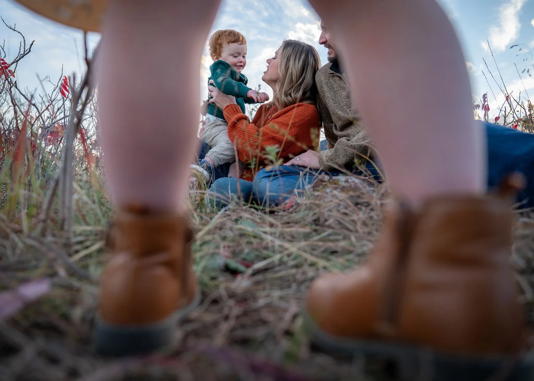 A creative family portrait of mom playfully lifting her young son up in the air photographed through her daughters legs. A fun, natural family photo session at South Mesa Trailhead in Boulder, Colorado captured by Ryan Kost
