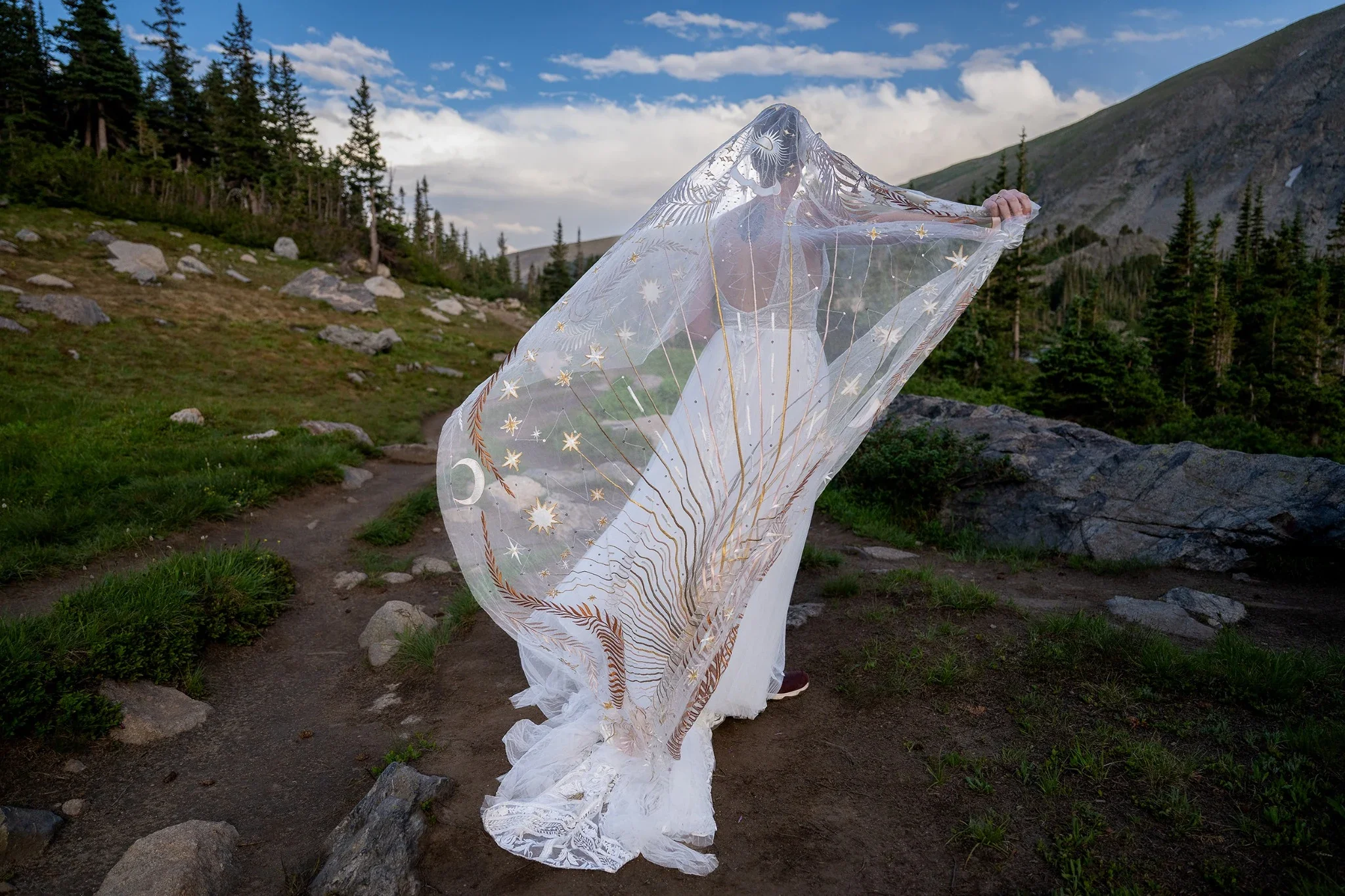 Bride standing beneath embroidered celestial veil during intimate hiking elopement in the Indian Peaks Wilderness near Lake Isabelle, Colorado