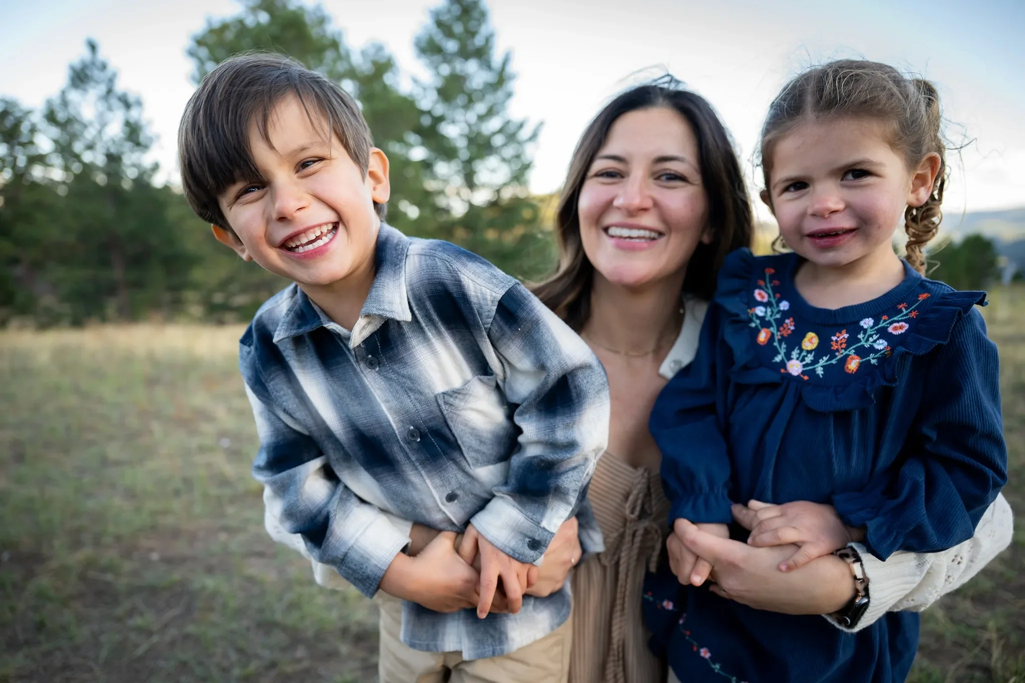 Mom holding her son and daughter tightly sharing laughter during a joyful, loving family photo session at Mount Falcon West captured by Denver family photographer Ryan Kost.