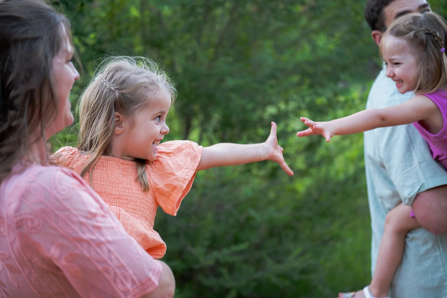 Sweet candid moment between two sisters reaching for each other across their parents’ arms during a family session at Red Rocks Canyon Open Space in Colorado Springs captured naturally by Ryan Kost