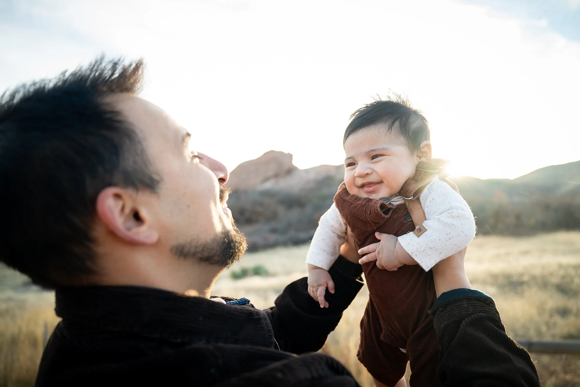 An infant portrait with his adorable smile as dad lifts him up in the air.  Natural, timeless Colorado family photography captured by Ryan Kost