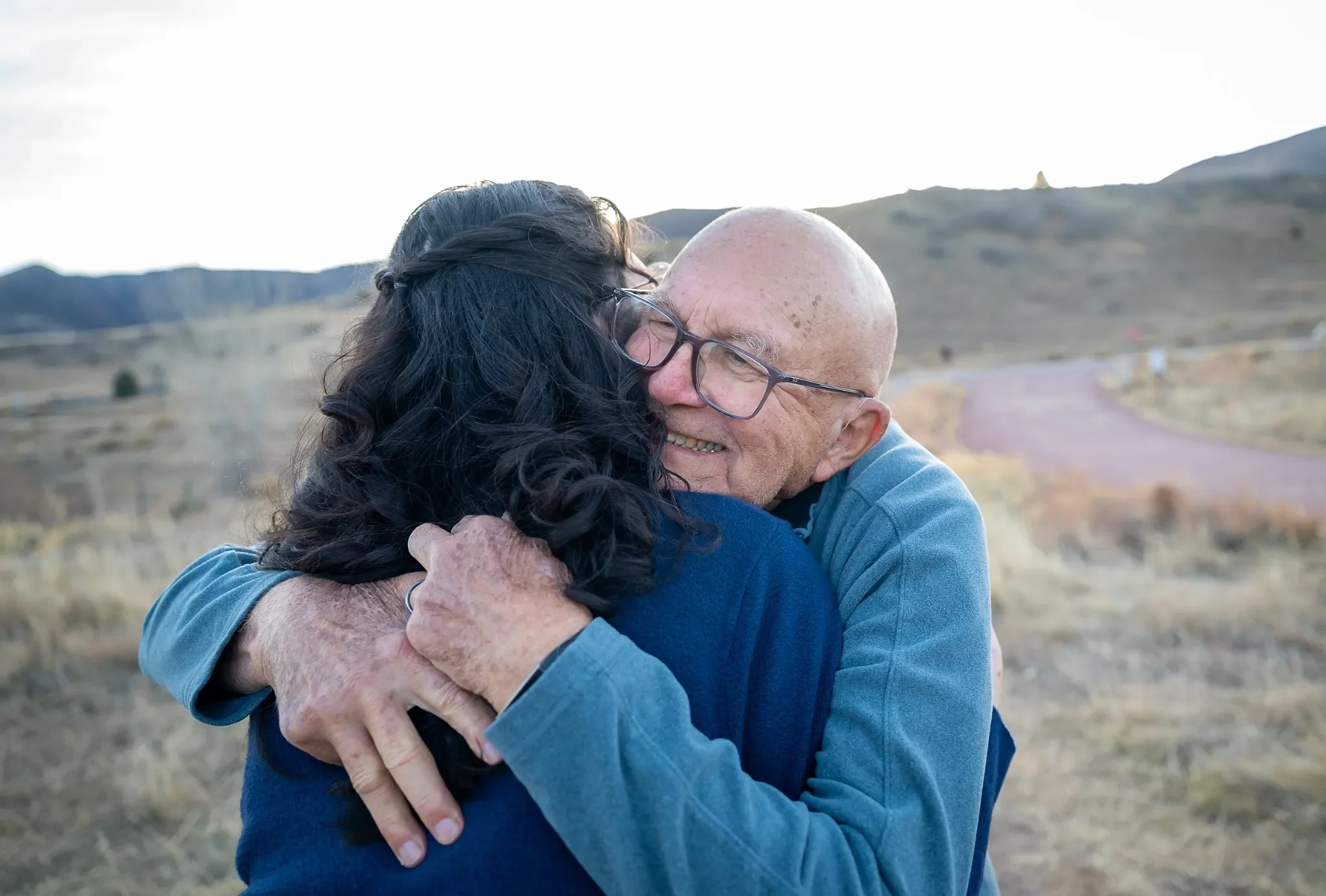 Daughter-in-law to be shares a warm hug with her fiance's grandfather after saying I do during a surprise proposal engagement at South Valley Park in Littleton, Colorado captured by Ryan Kost.