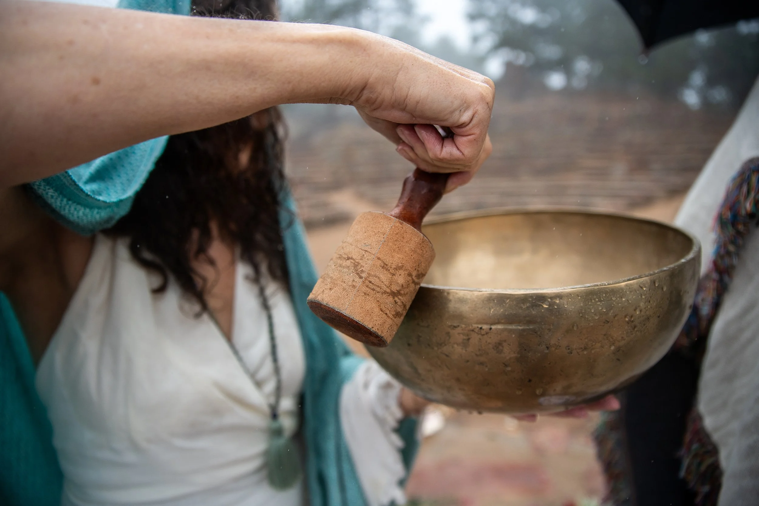 Close-up of a person holding a mallet and striking a singing bowl, outdoors in a foggy environment.