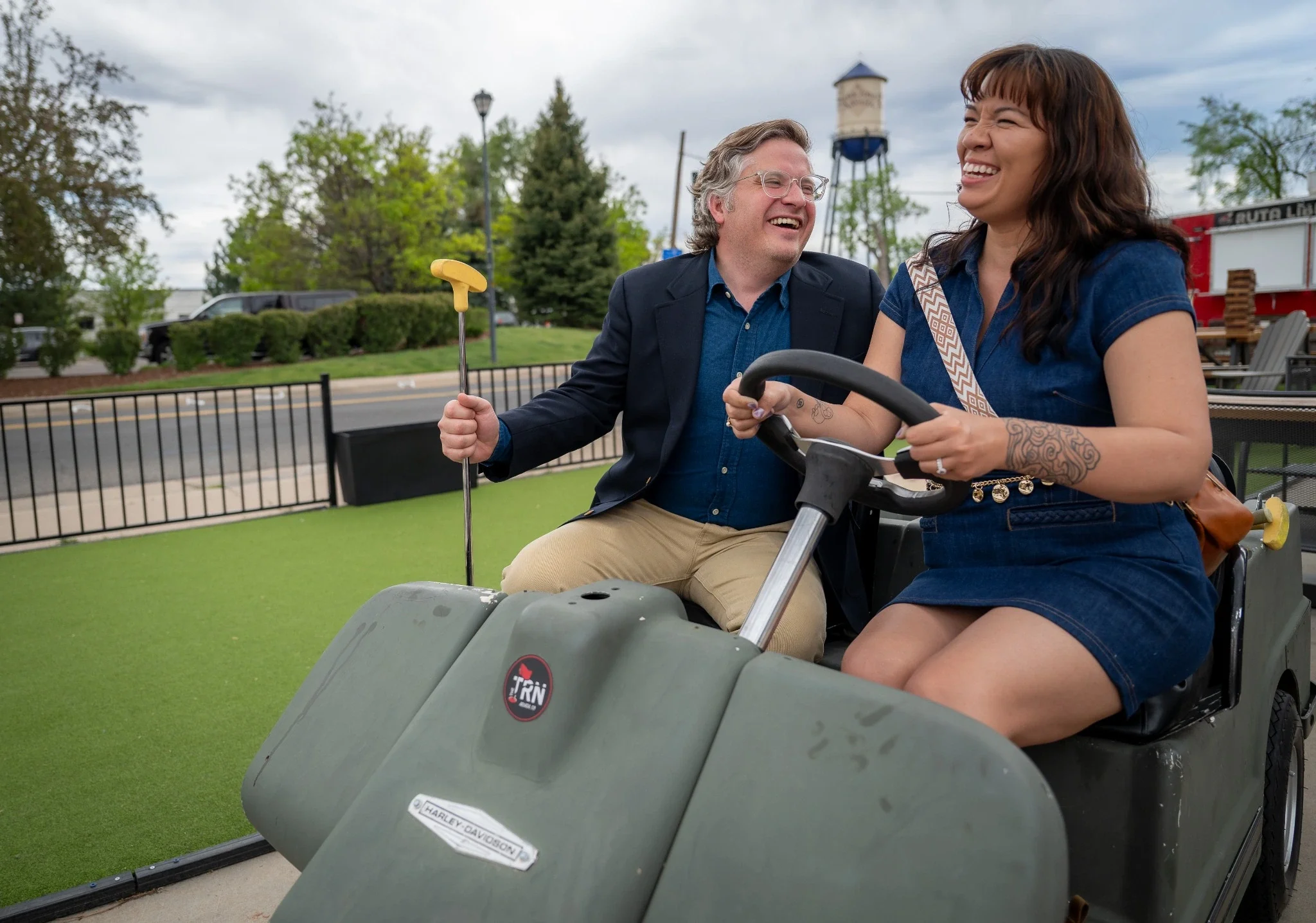 Romantic couples photo session in Olde Town Arvada, Colorado featuring a laughing couple riding a golf cart during a playful downtown engagement photography session by Ryan Kost Photography.