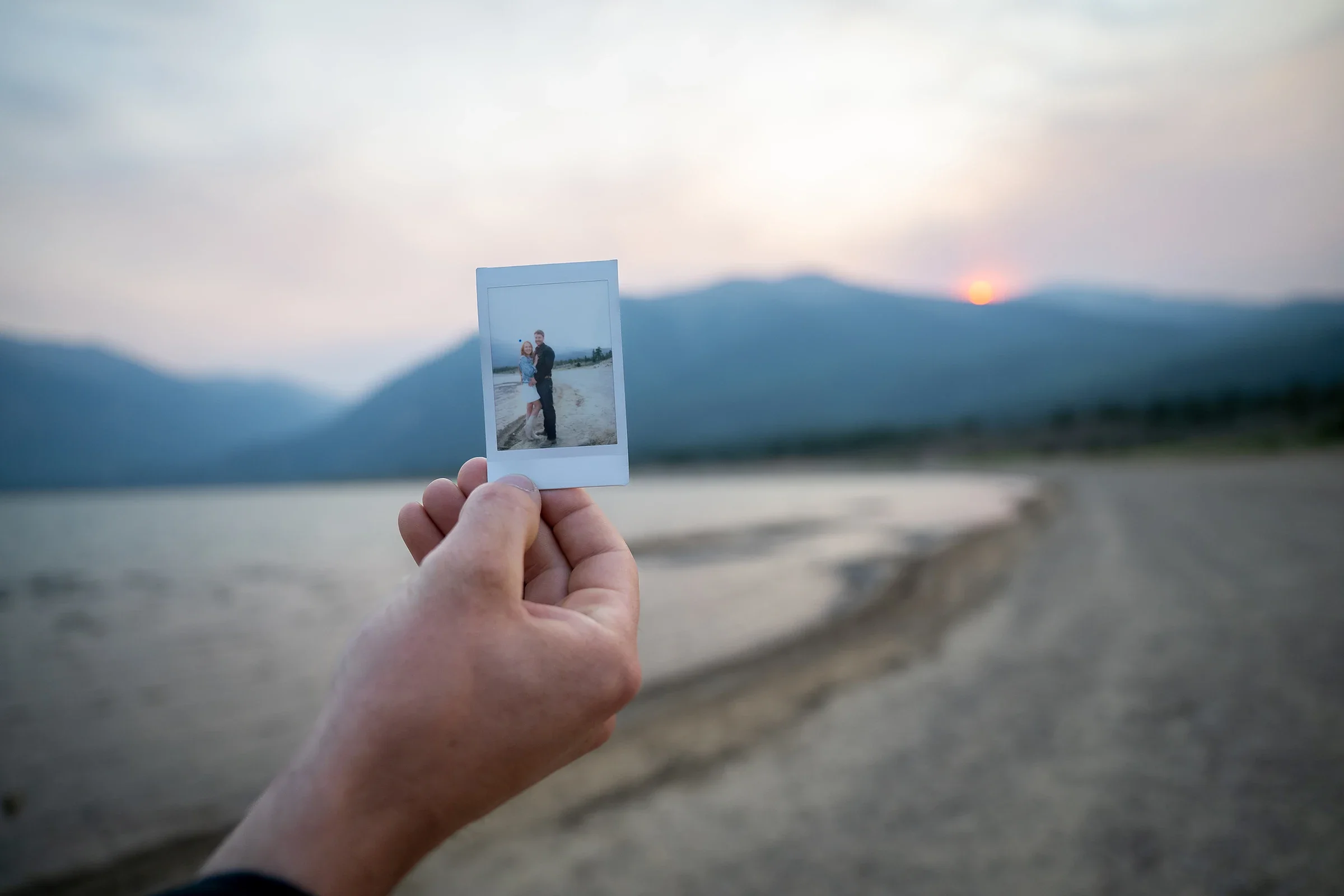 Bride holding a Polaroid photo with Twin Lakes and the Colorado mountains in the background.