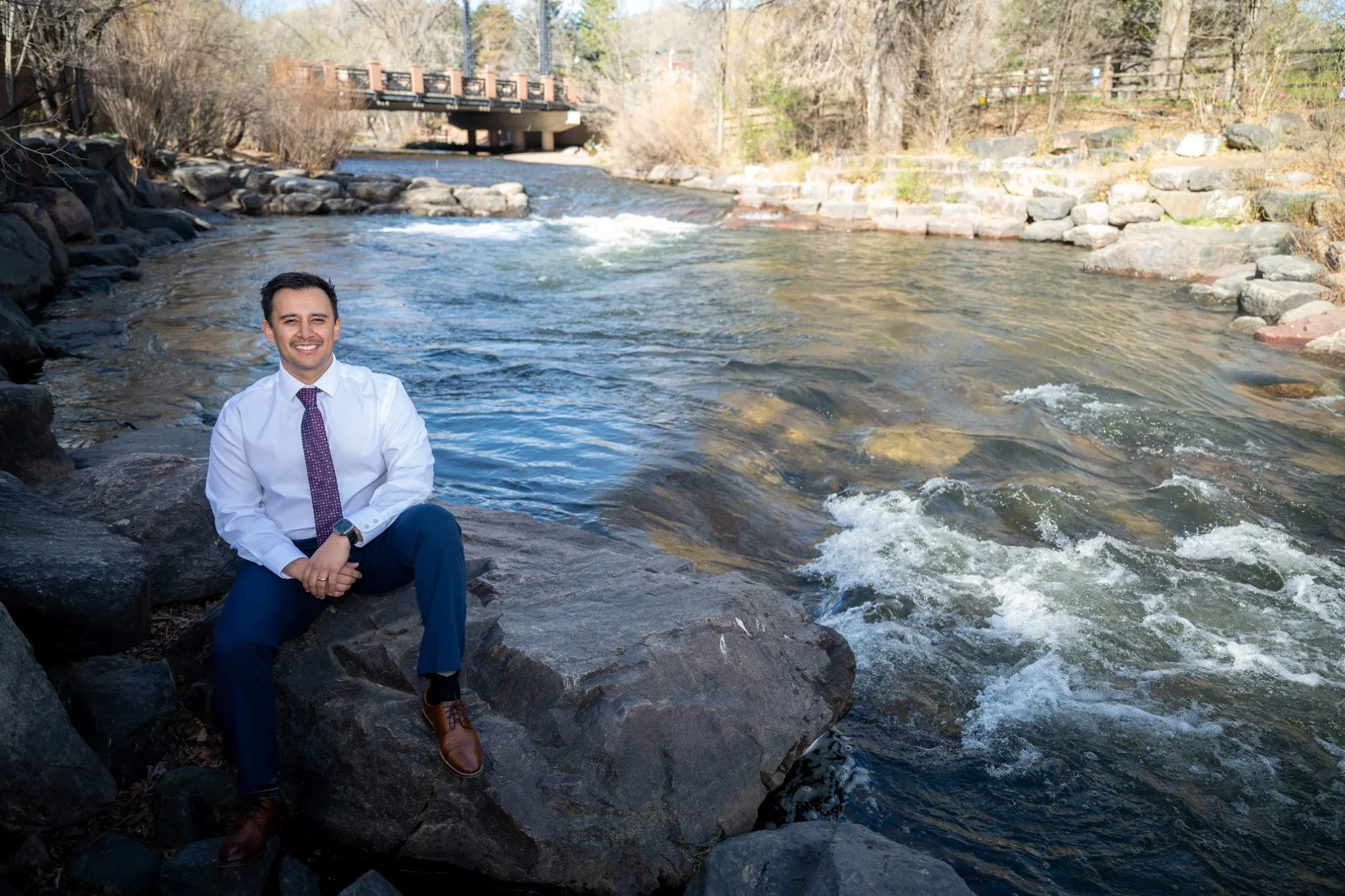 Relaxed professional business headshot portrait photography sitting outdoors on rocks at Clear Creek in downtown Golden Colorado
