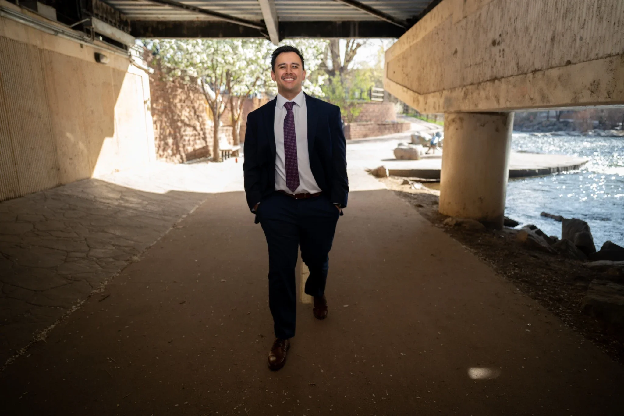 Relaxed, outdoor professional business portrait photography walking under bridge beside Clear Creek in Golden, Colorado.