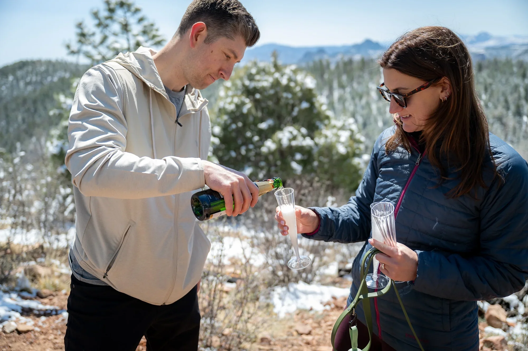 Pouring champagne for newly engaged couple celebrating on hike in Conifer, Colorado.