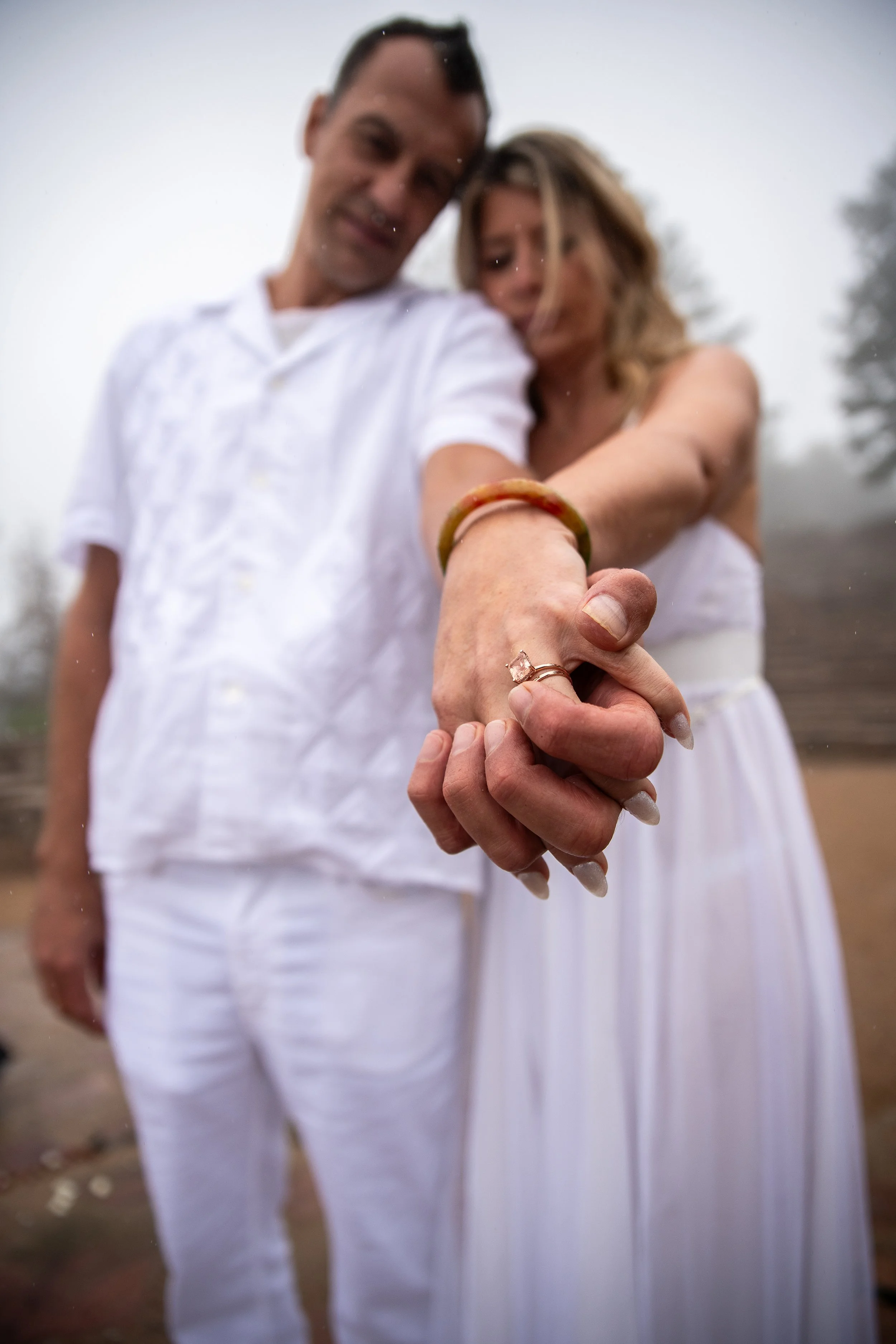 A couple holding hands outdoors, showing their wedding rings, with a focus on their hands.