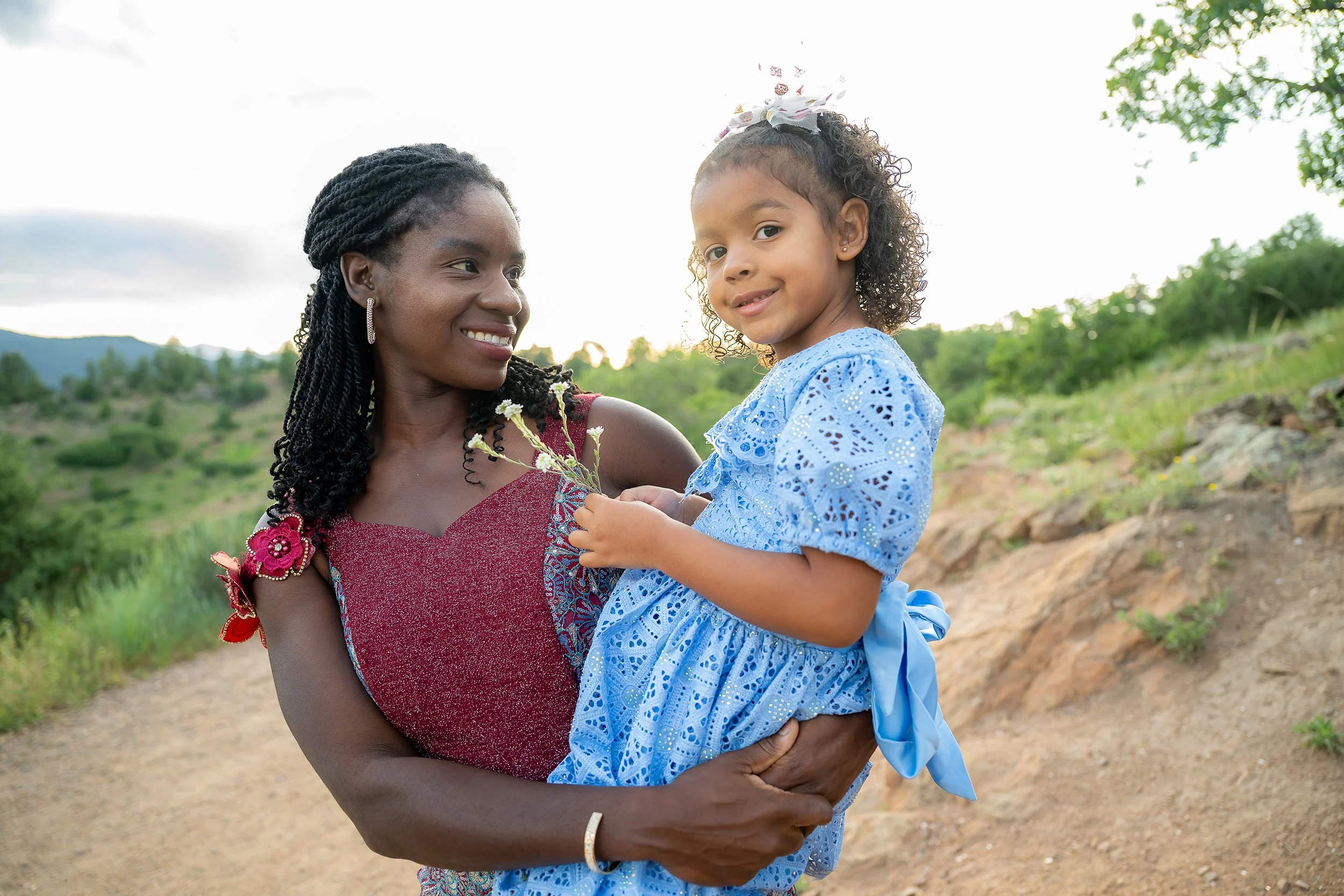 Mom lovingly holds and looks at daughter. Natural, candid outdoor family portrait photography at Mount Falcon West in Colorado captured by Ryan Kost