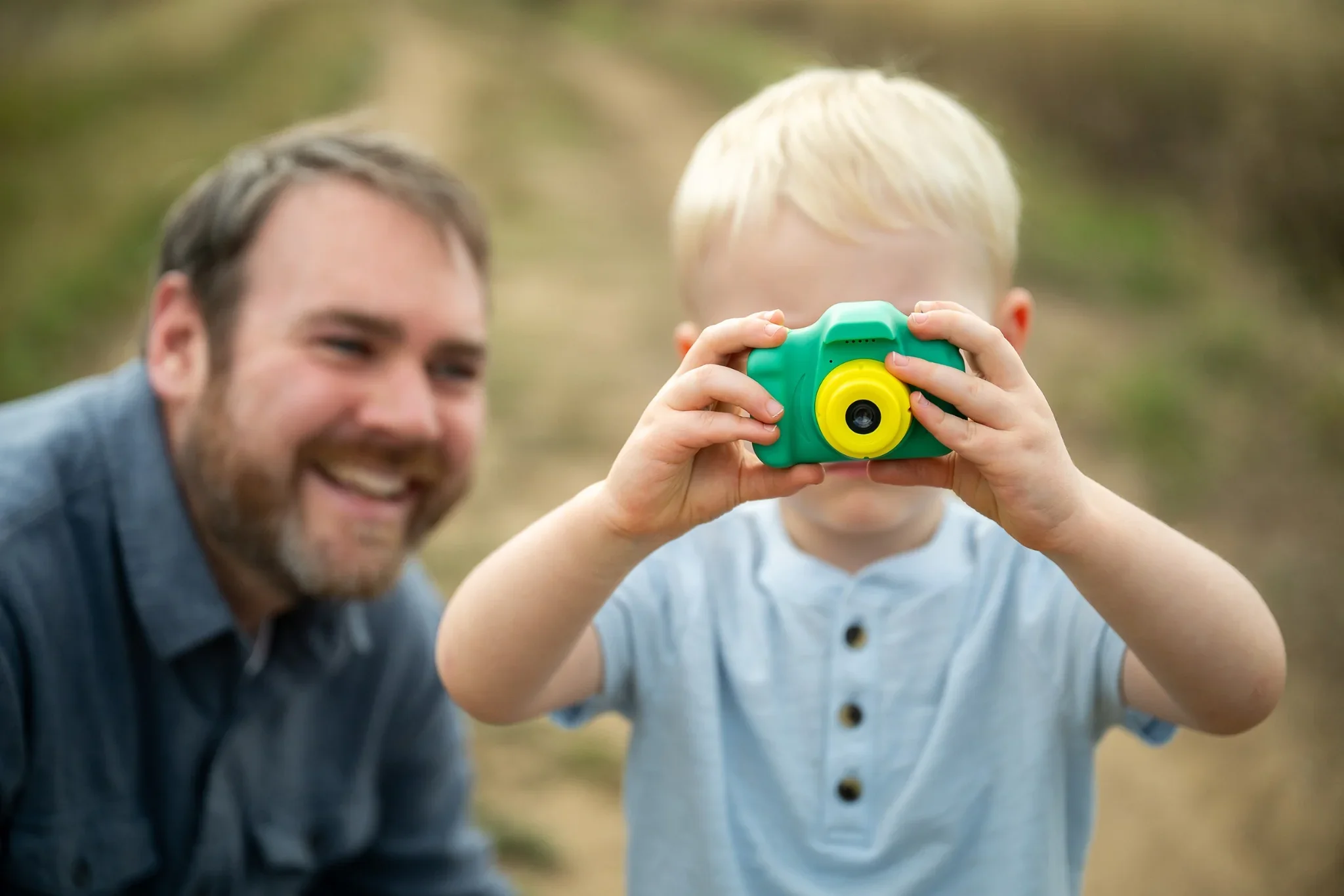 Boy takes a photo of me with his dad smiling behind him at Standley Lake in Westminster, Colorado.  Relaxed, natural family photography captured by Ryan Kost.