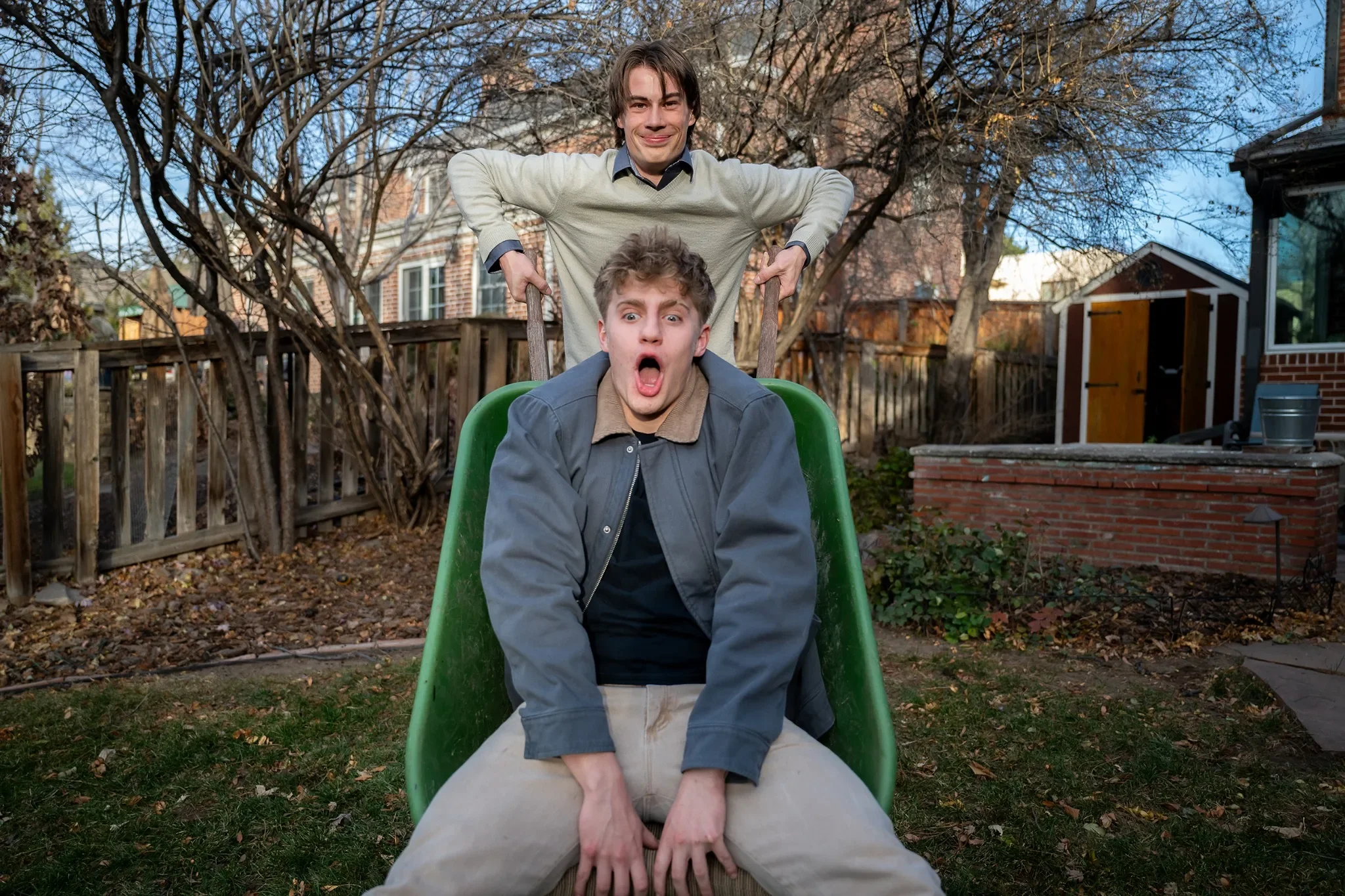 Boys will be boys. Teenage cousins portrait playing in backyard tipping each other over in wheelbarrow. Documentary family photography captured by Denver photographer Ryan Kost.