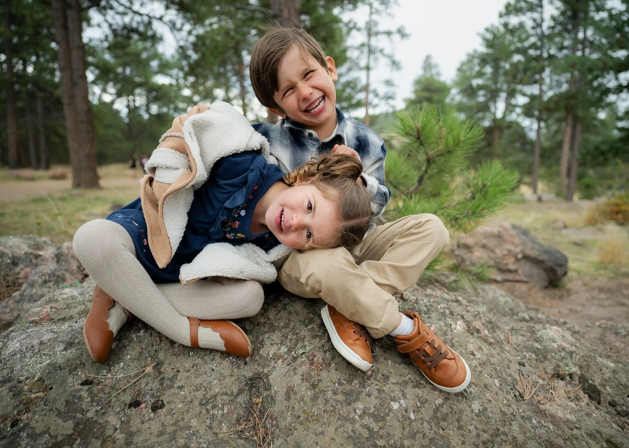 Brother and sister adorable portrait sitting on rock outcropping at Mount Falcon West Trailhead in the Denver Foothills. Relaxed, joyful outdoor family photography captured by Ryan Kost