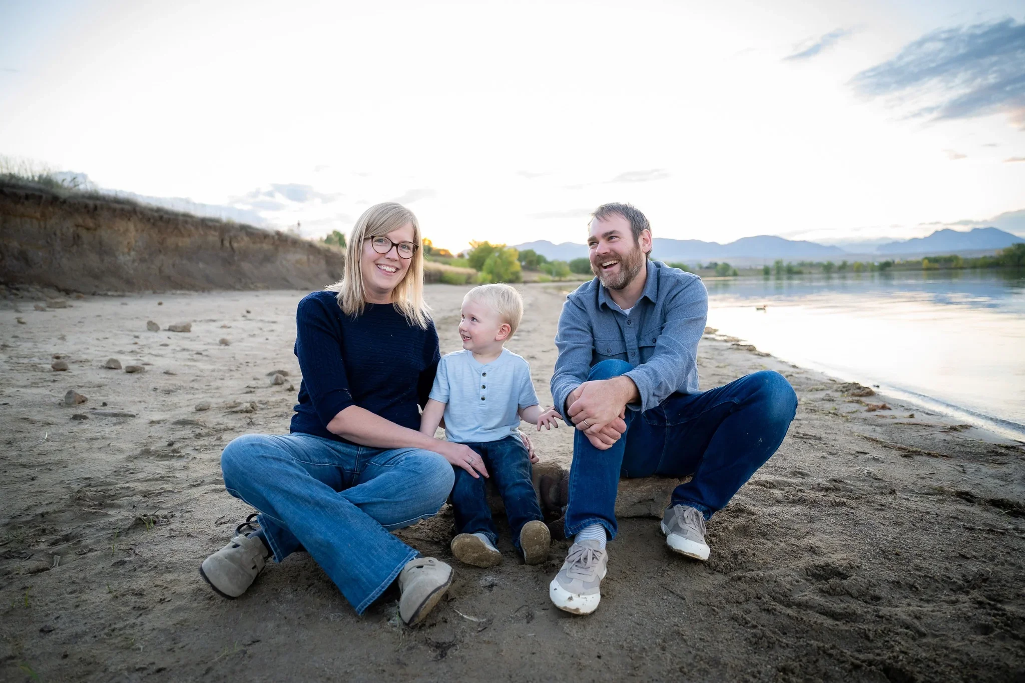 Family sitting on sandy shoreline at Standley Lake in Westminster, Colorado. Relaxed, natural family photography captured by Ryan Kost