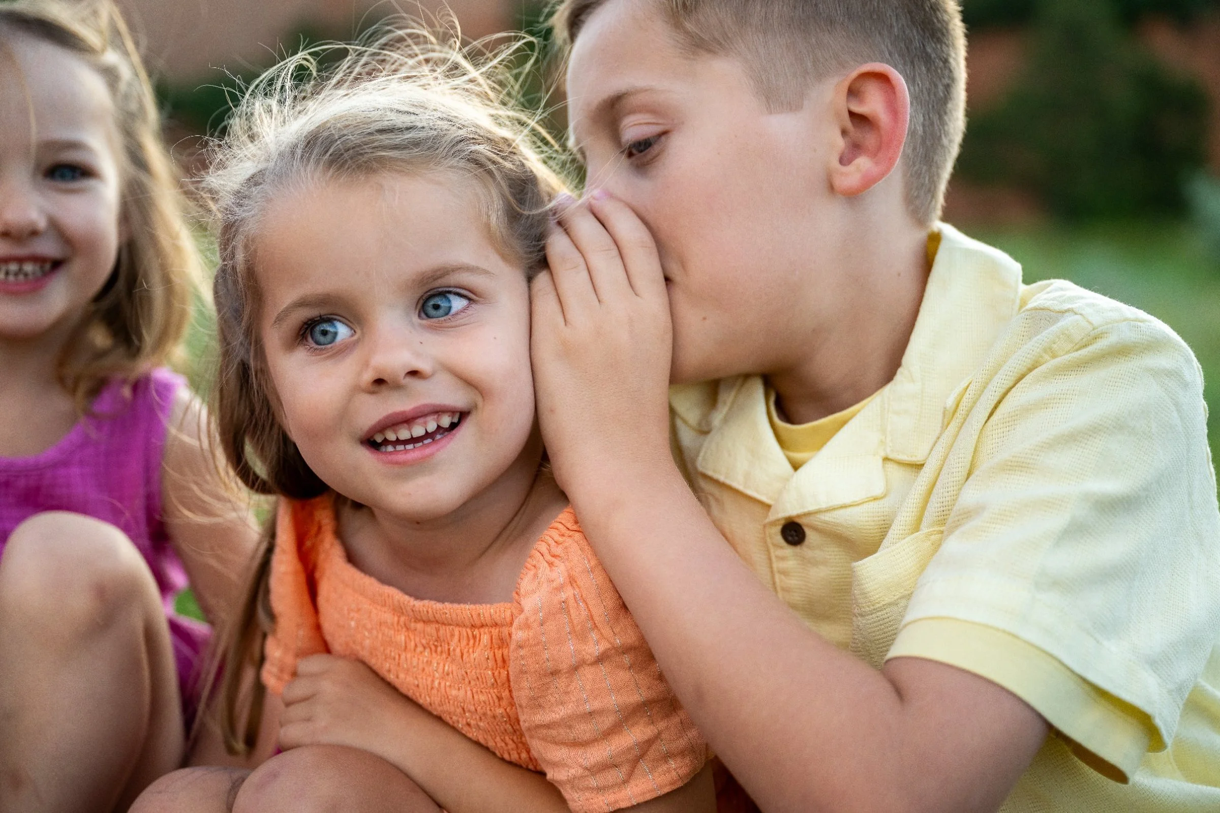Siblings whispering secrets in a fun game of telephone. Candid, natural family photography captured by Ryan Kost at Red Rock Canyon Open Space in Colorado Springs.