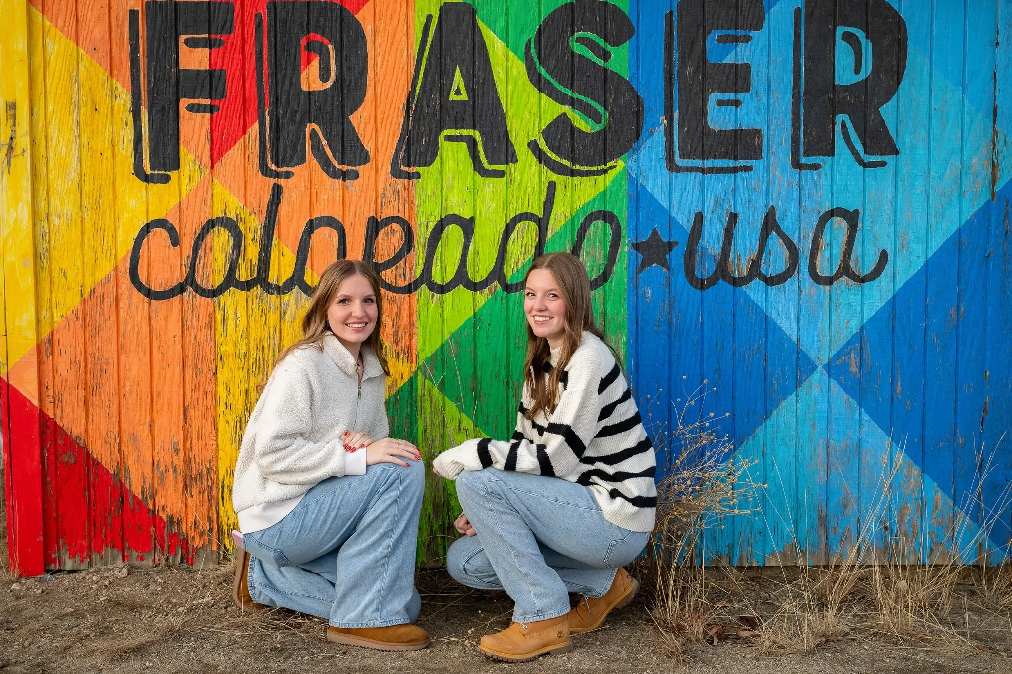Sisters family portrait in front of colorful Fraser, Colorado sign captured during a winter photo session by Ryan Kost.