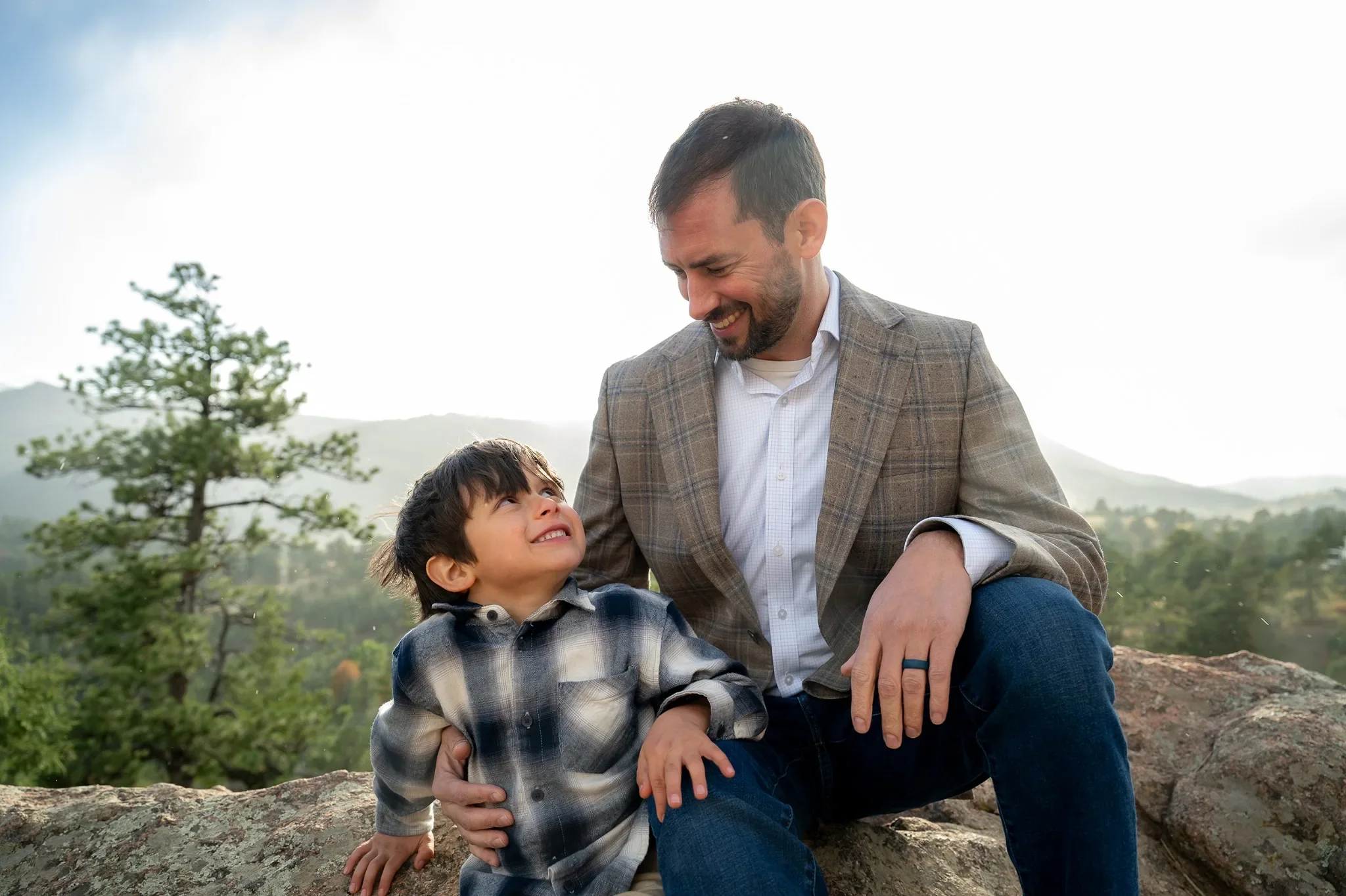 A cute portrait with dad and son sitting on rock outcropping sweetly looking at each other.  Mount Falcon West, Colorado family photography captured by Ryan Kost.