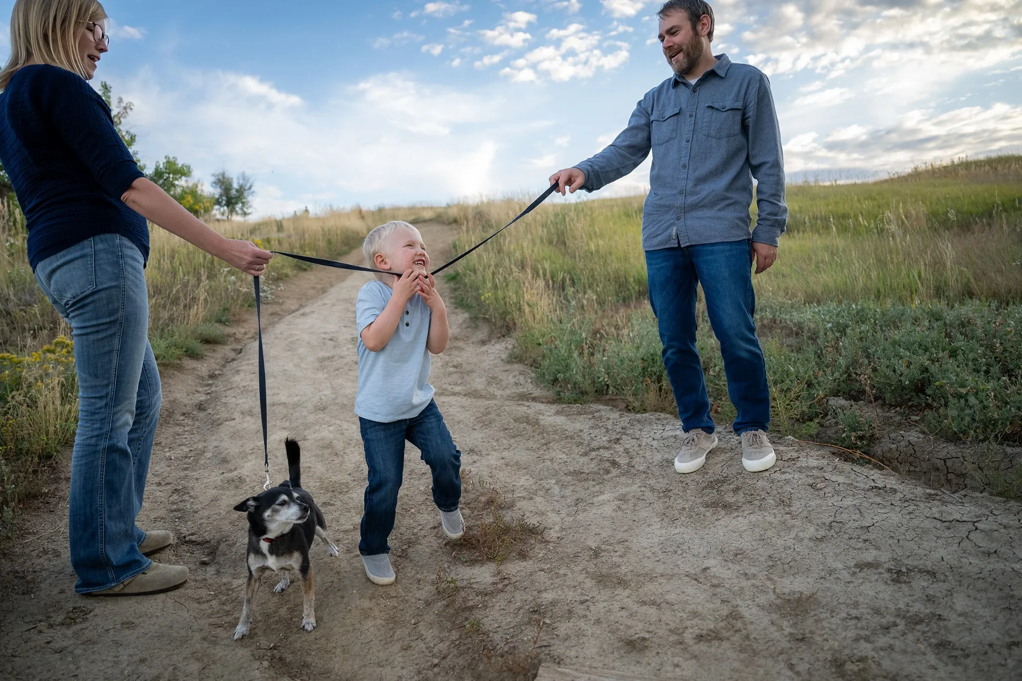 A family playing a fun game of limbo with dog leash at Standley Lake in Westminster, Colorad.  Relaxed, natural family photography captured by Ryan Kost.