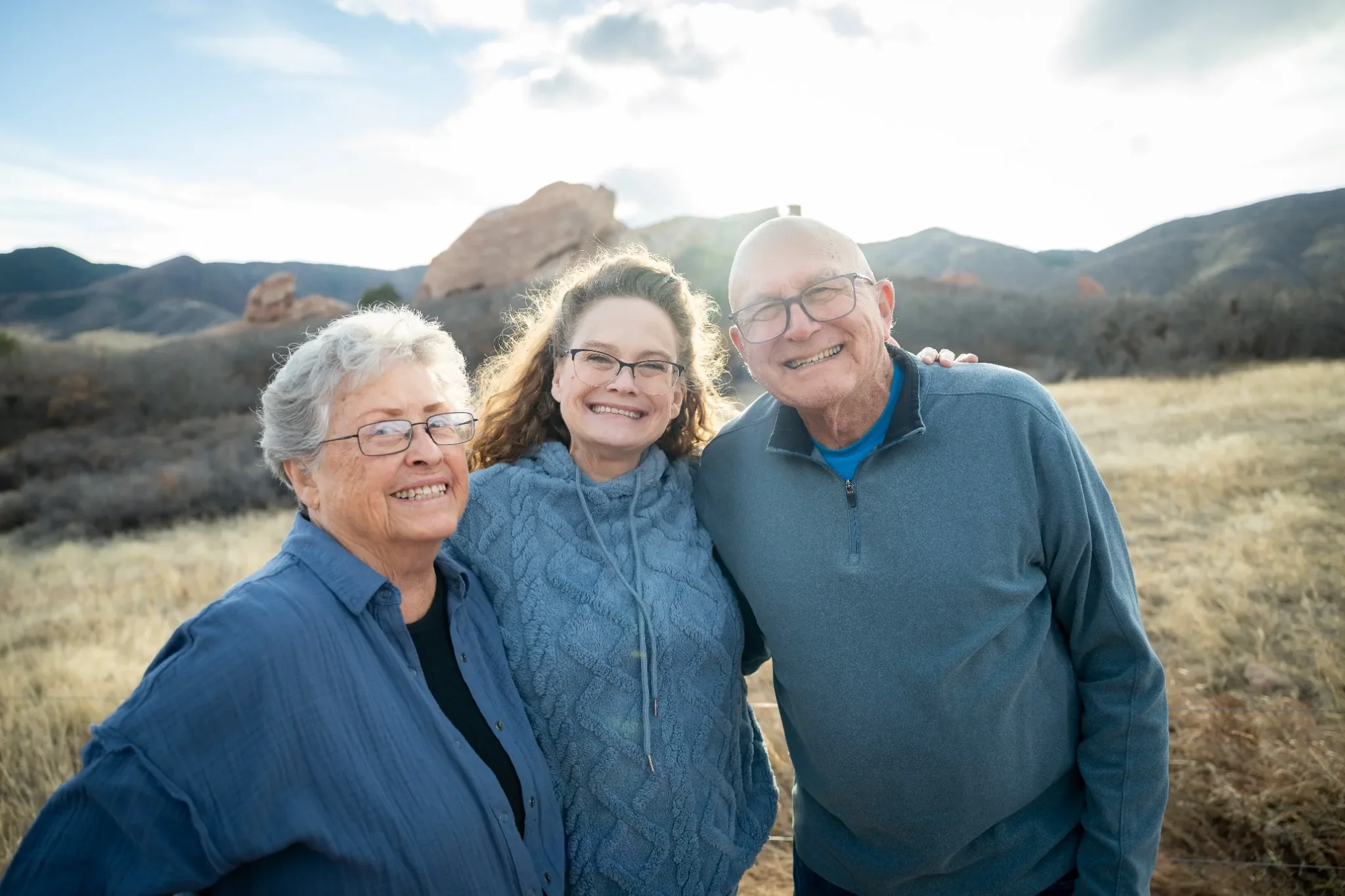 Parents with daughter and red rocks framed behind during a golden hour winter family photo session at South Valley Park in Littleton, Colorado captured by Ryan Kost.