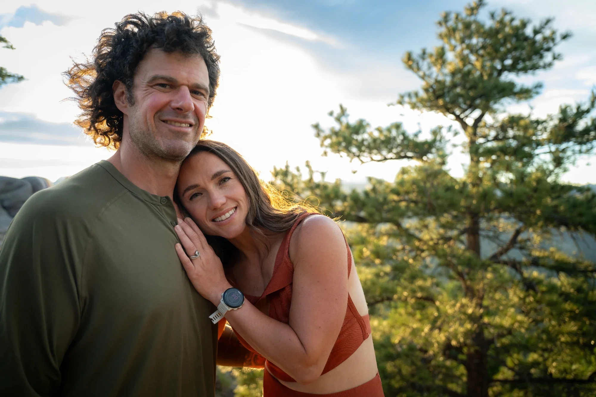 Couple embracing during a golden hour photo session at Lost Gulch Overlook in Boulder, Colorado with warm summer light and pine trees.
