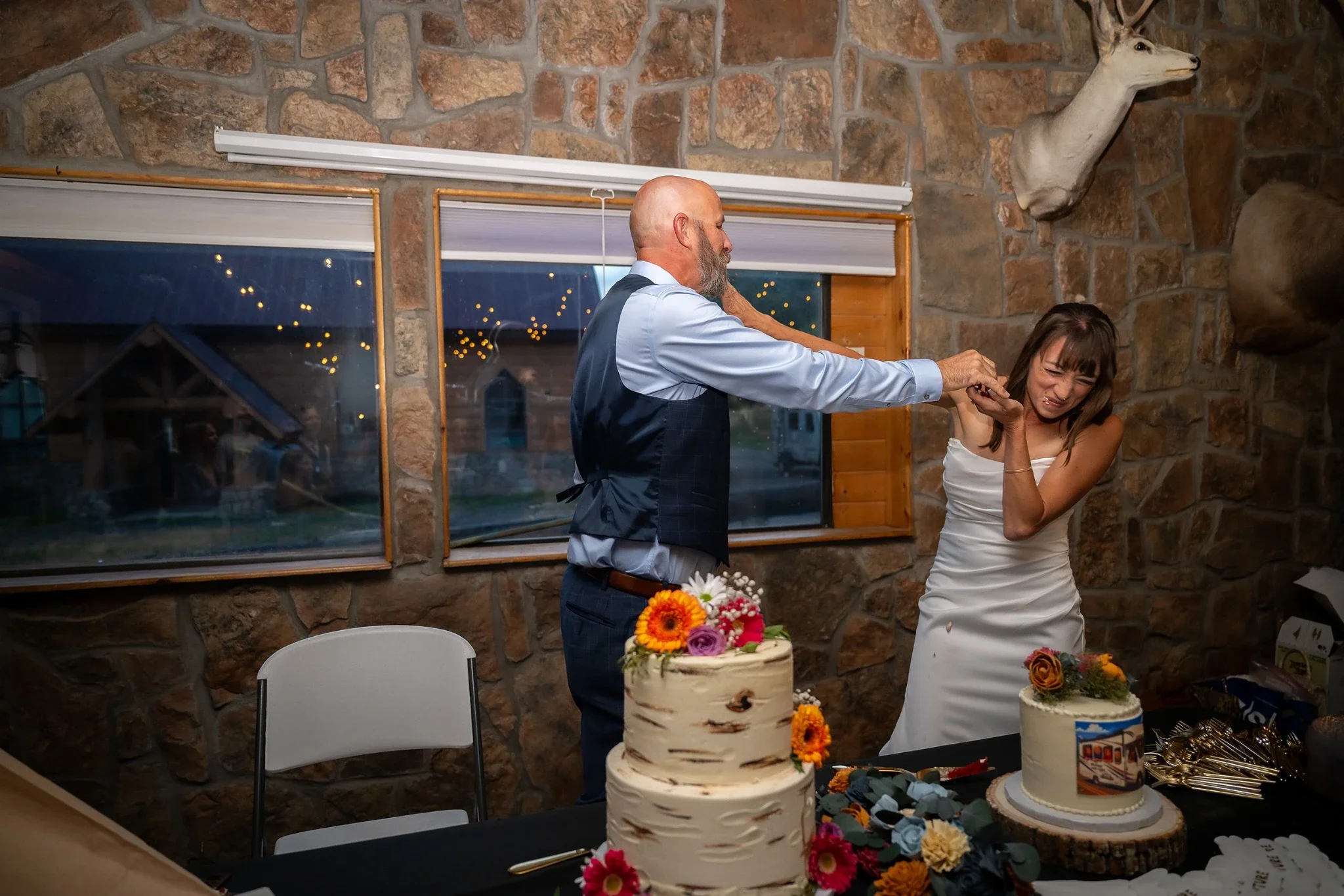 Bride and Groom smashing cake against each other's faces at Red Bear Haus in Horca, Colorado at wedding reception.