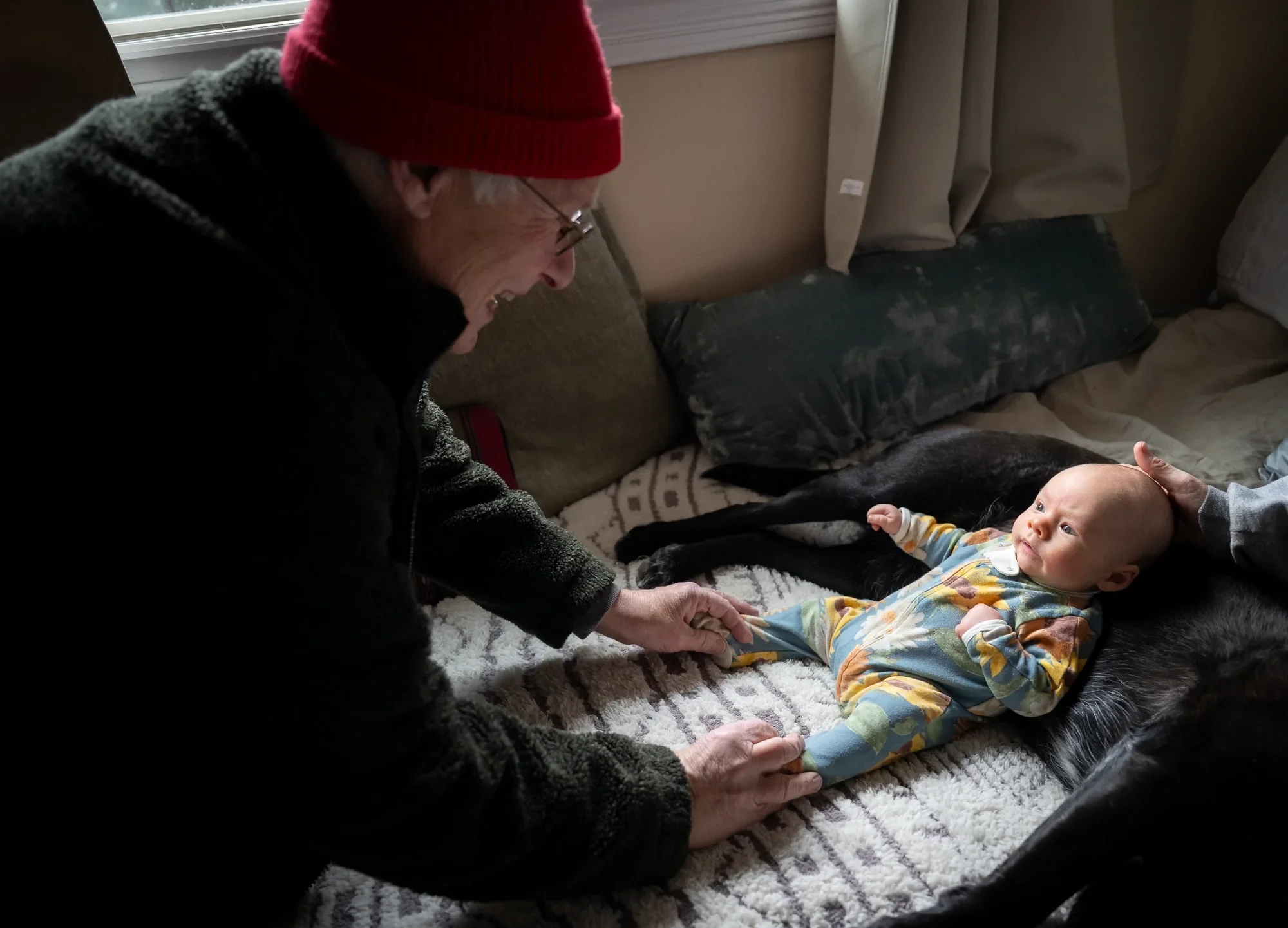 Grandfather tickling toes of newborn grandson captured during an in home documentary family session in Arvada, Colorado