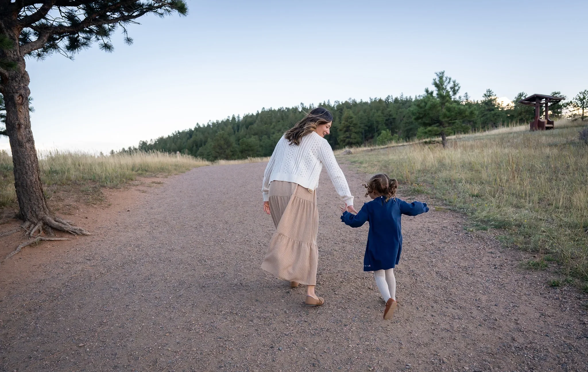 Mom & daughter running down the path together holding hands captured during a loving & natural outdoor family photo session at Mount Falcon West trailhead in the Denver foothills. Ryan Kost Photography.