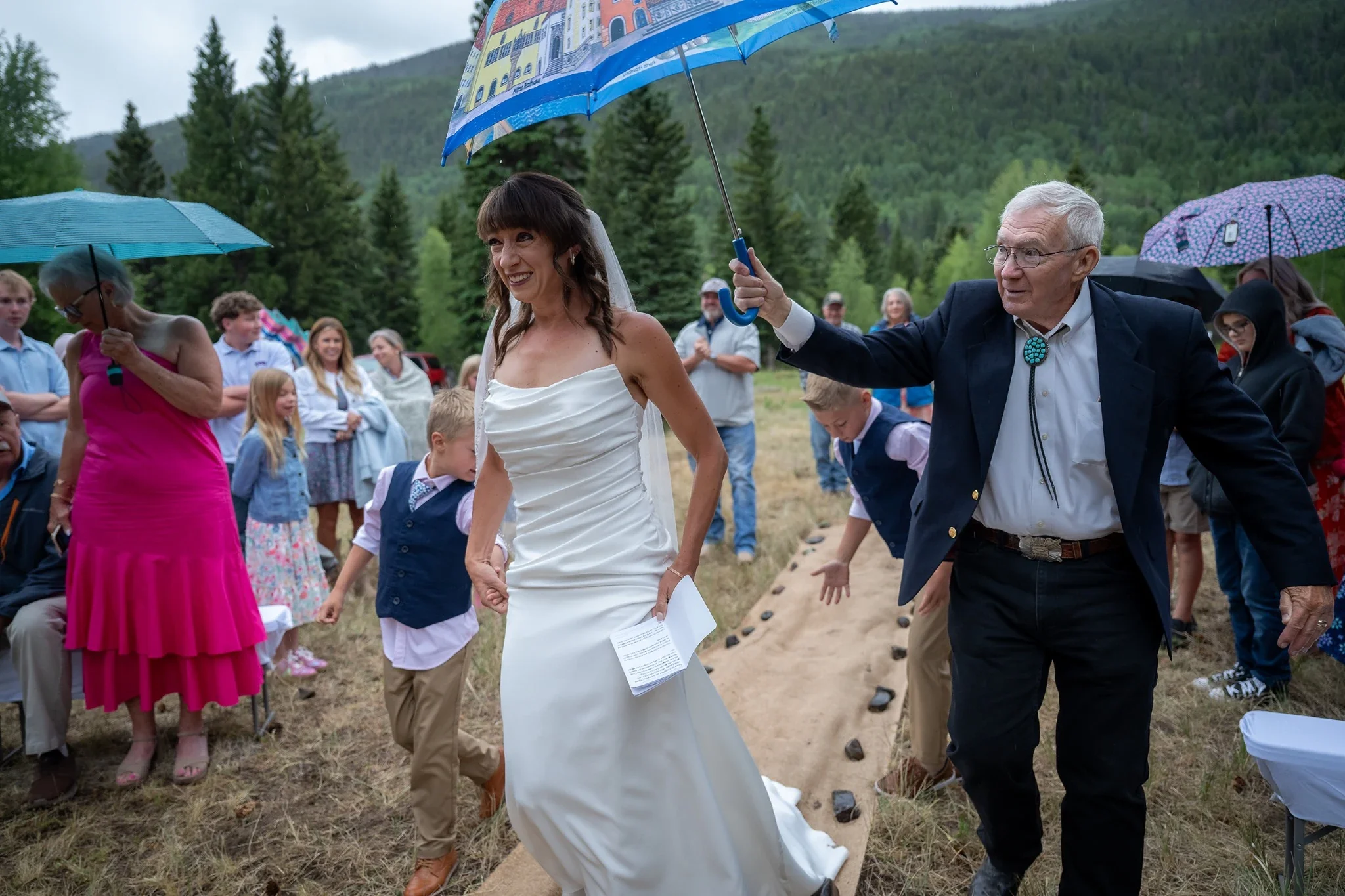 Dad walks his daughter down the aisle at her wedding on a rainy summer ceremony at Spectacle Lake Campground in Horca, Colorado.
