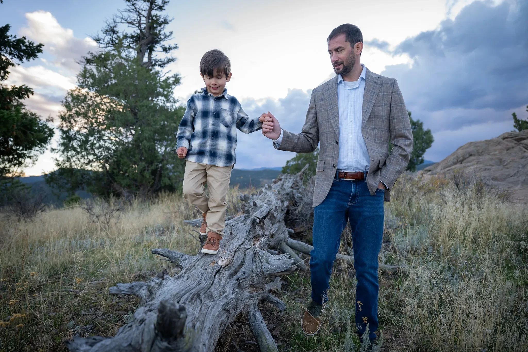 Dad holds his sons hand as he balances on a downed tree on the trail at Mount Falcon West Trailhead in the Denver Foothills. Relaxed & natural family photography captured by Ryan Kost