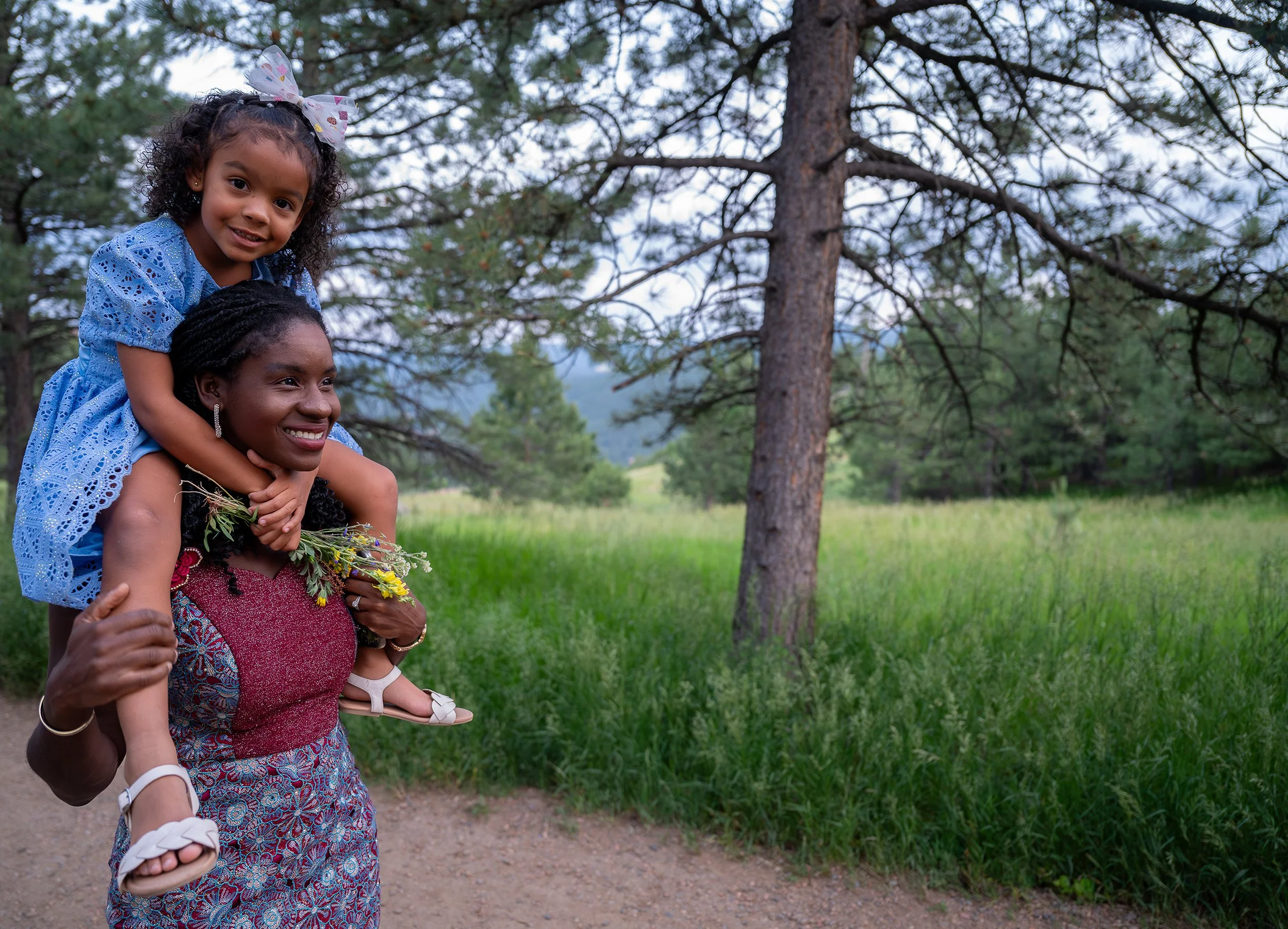 All smiles as mom carries daughter on her shoulders on trail at Mount Falcon West Trailhead in Colorado. Captured by Denver family photographer Ryan Kost.
