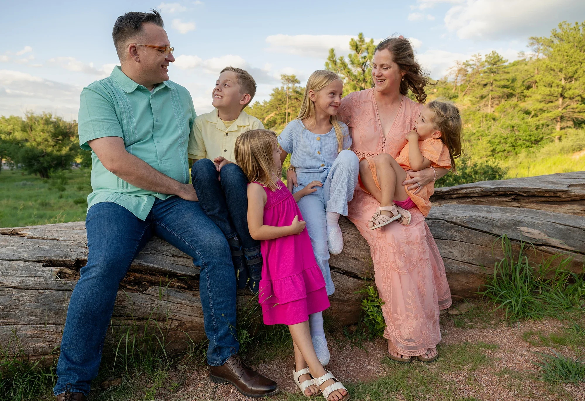 A vibrant, joyful family portrait sitting together on an old log at Red Rock Canyon Open Space in Colorado Springs. Natural, relaxed family photogrraphy captured by Ryan Kost