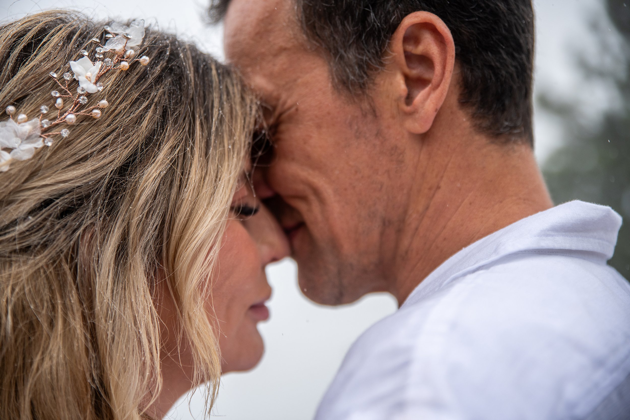 Close-up of a couple with their foreheads touching, smiling softly, outdoors on a cloudy day.