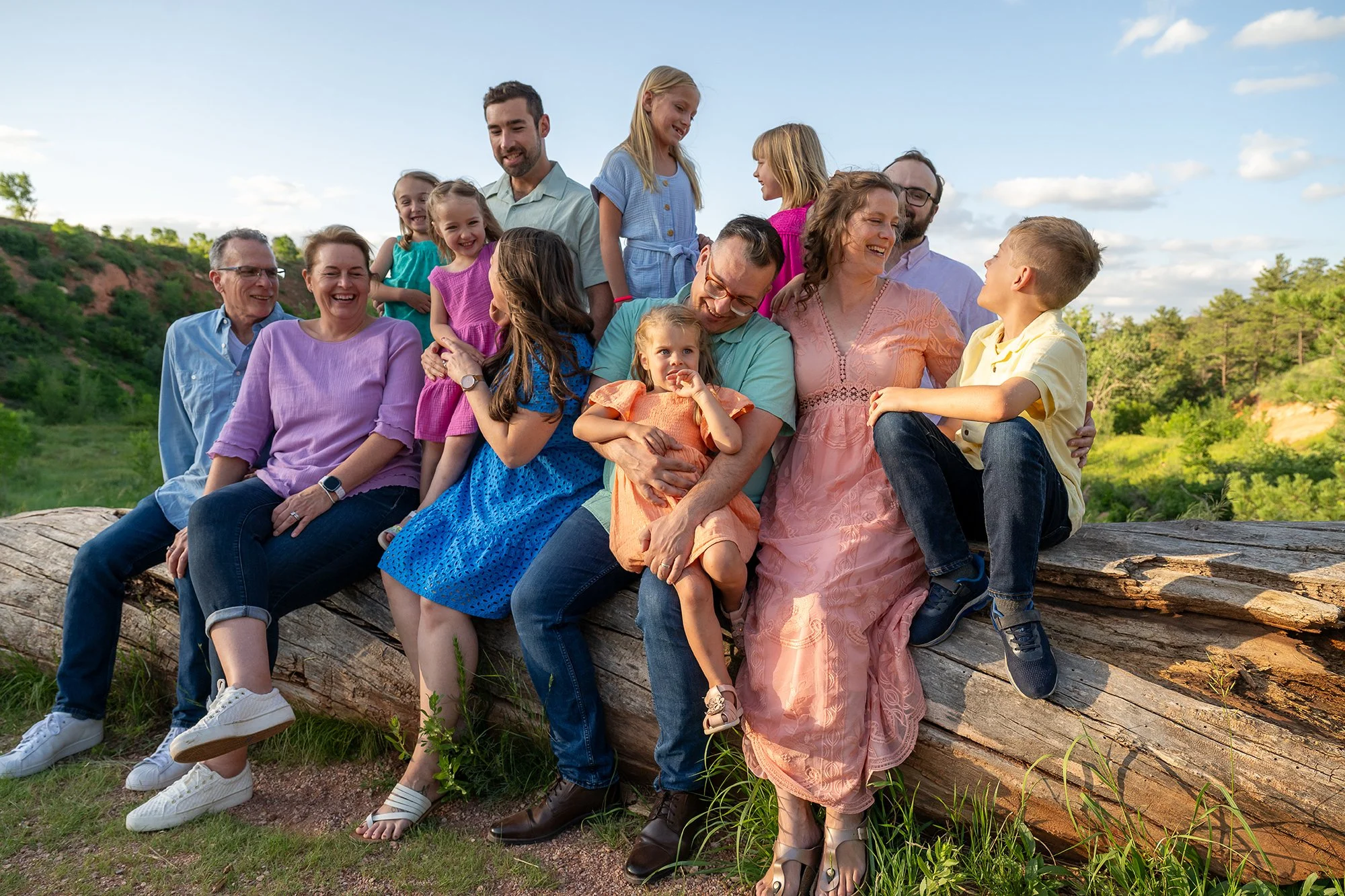 Vibrant, multi-generational family laughing together on a log during golden hour at Red Rock Canyon Open Space in Colorado Springs, captured by Ryan Kost Photography