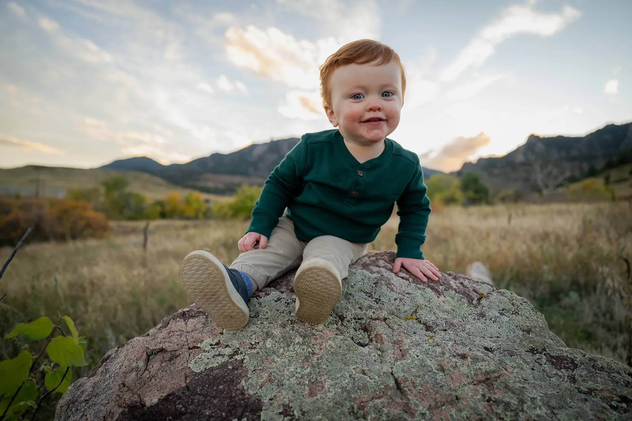 Cute, natural portrait of young boy sitting on rock with mountain views. South Mesa Trailhead in Boulder, Colorado. Ryan Kost family photography.