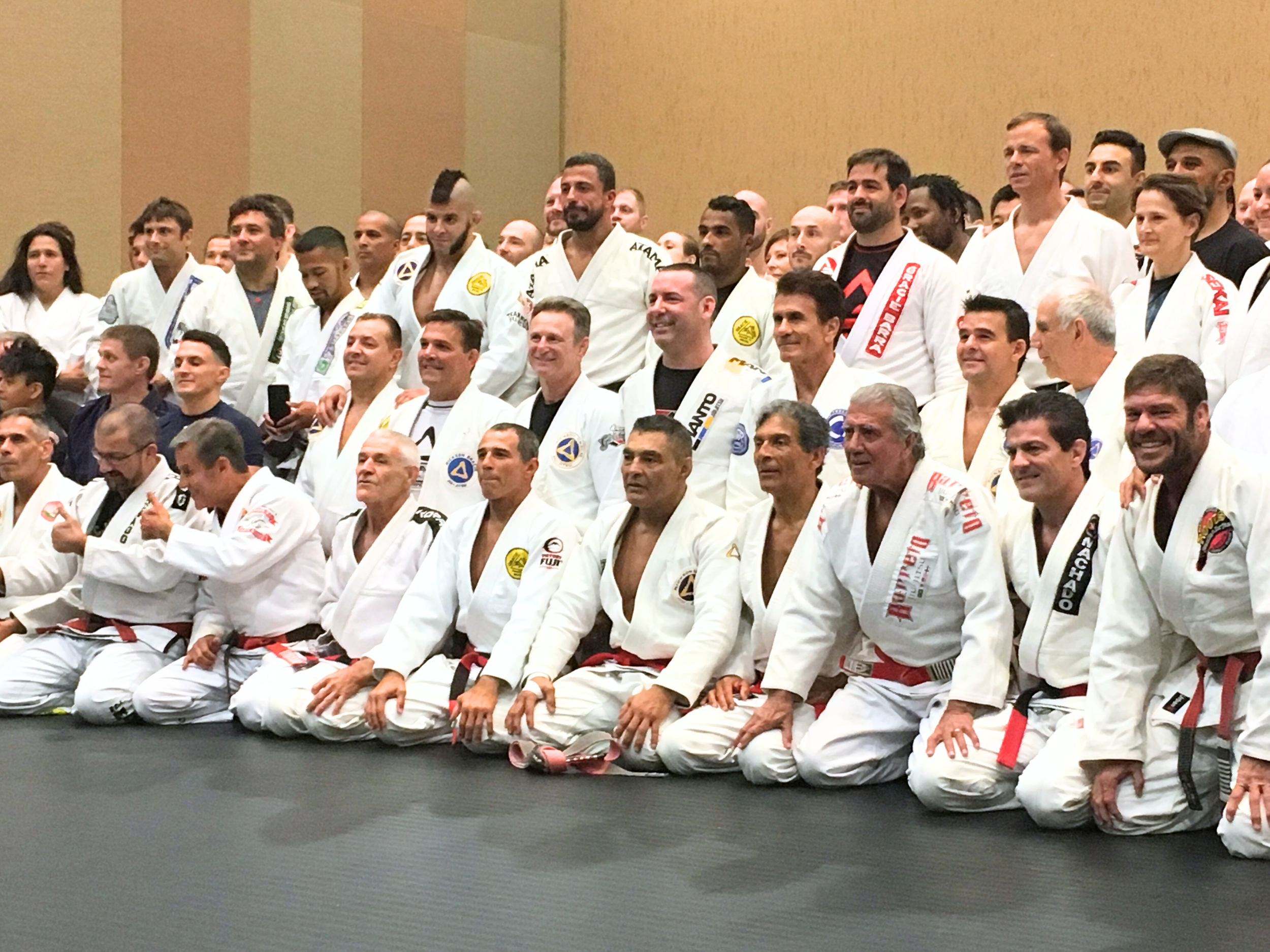 Group of diverse PDJ Jiu Jitsu practitioners in white belts and gis posing for a photo in a martial arts dojo.