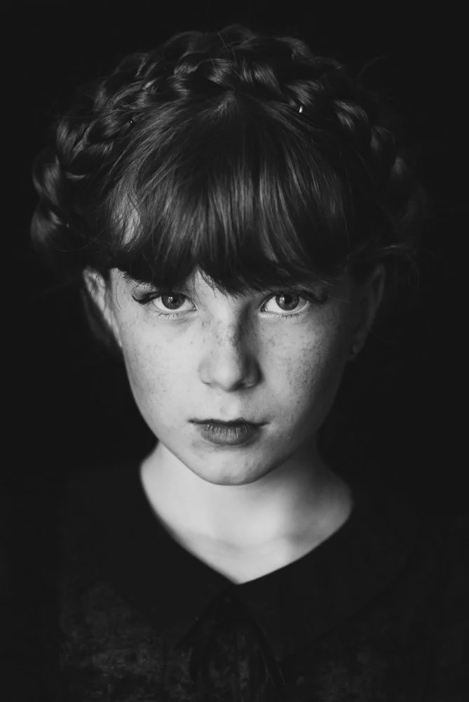 Portrait en noir et blanc d'une jeune femme avec des cheveux bouclés et une frange, regardant directement l'objectif.