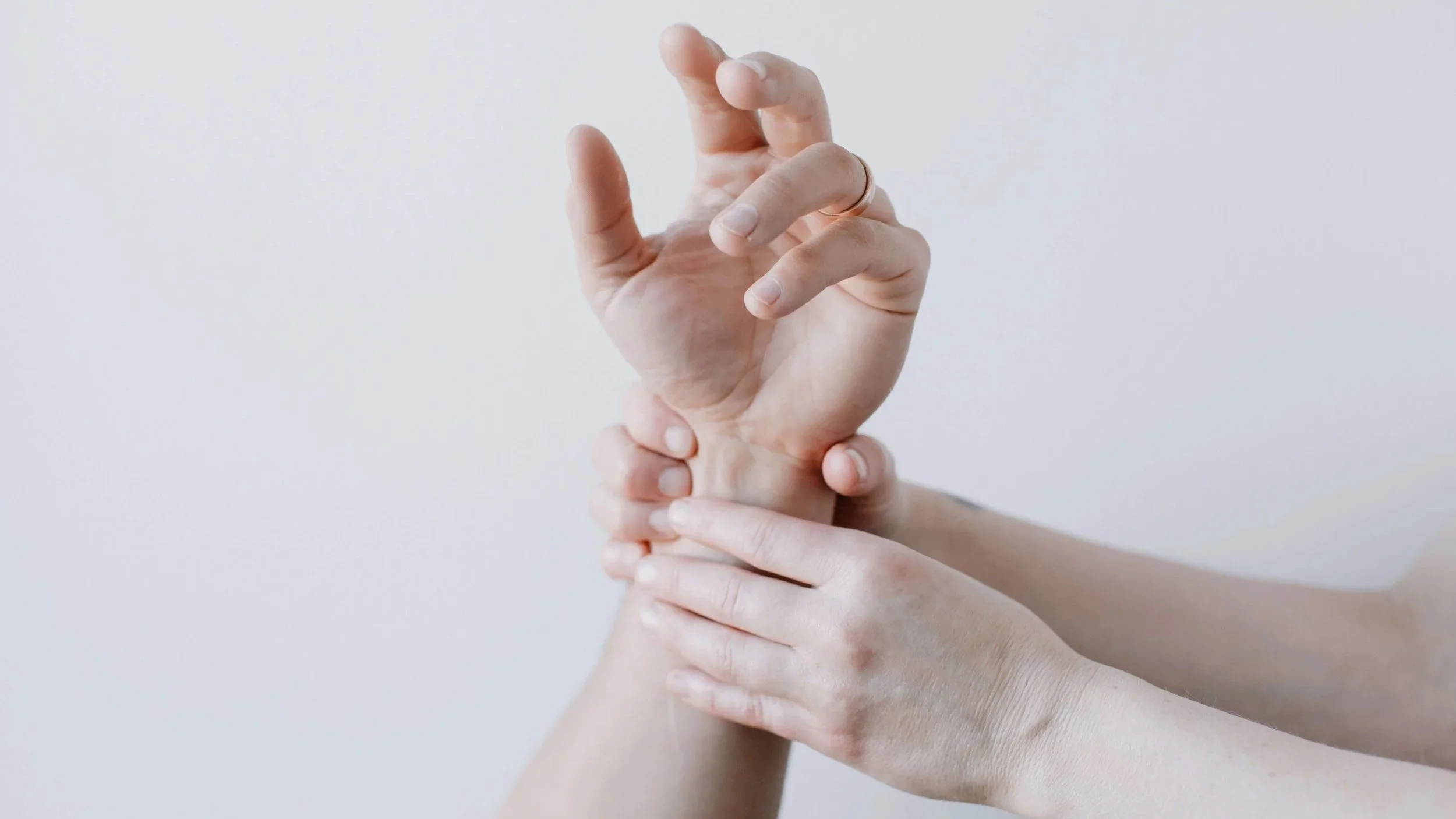 Two hands holding and supporting a person's wrist and hand, with a plain background.