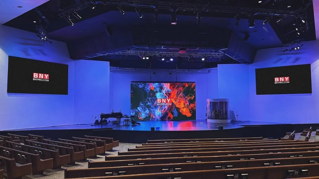 Empty auditorium with a stage, two large screens showing BNY logo, and a colorful digital display in the center.